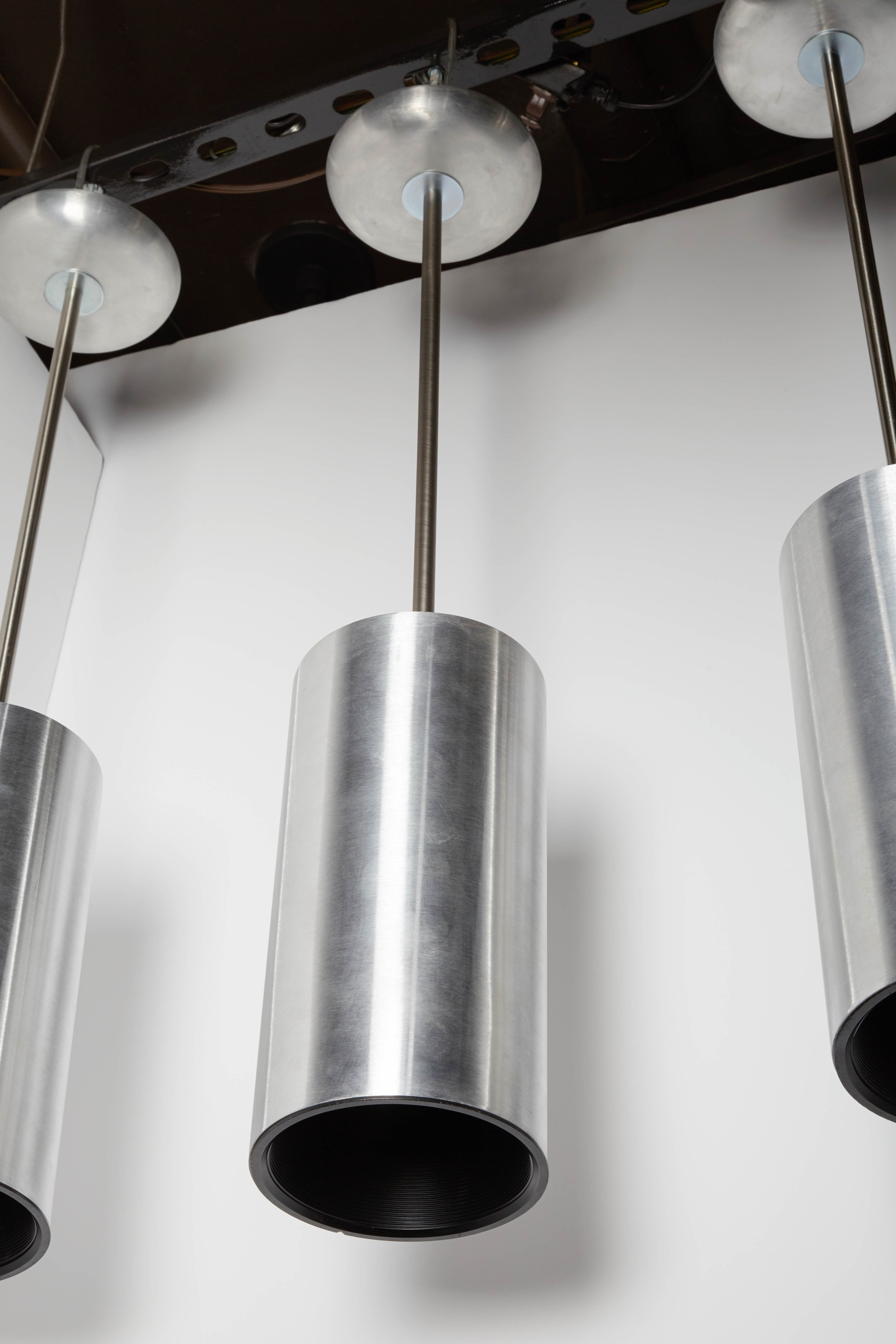 Set of three pendant fixtures with sleek cylinder Danish modern inspired forms. Comprised of brushed aluminum exteriors, ideal for a variety of contemporary, Mid-Century, or modern spaces. The pendants feature metal rods and matching aluminum