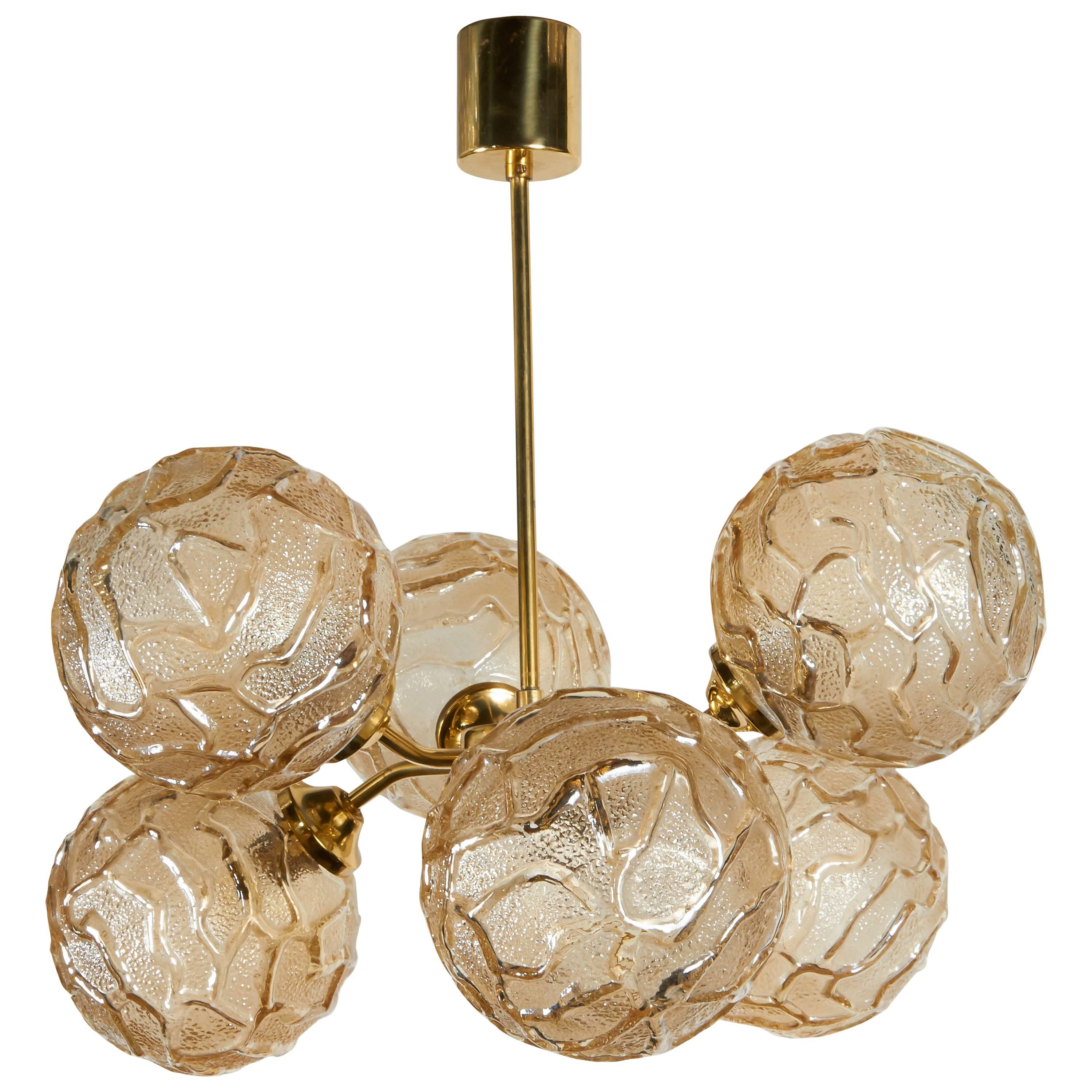 Mid-Century Modern Sputnik globe chandelier. The fixture has brass atomic frame with an elegant stem and cylinder canopy and features alternating arm design. Fitted with six textured art glass globes with geometric patterns in hues of champagne or