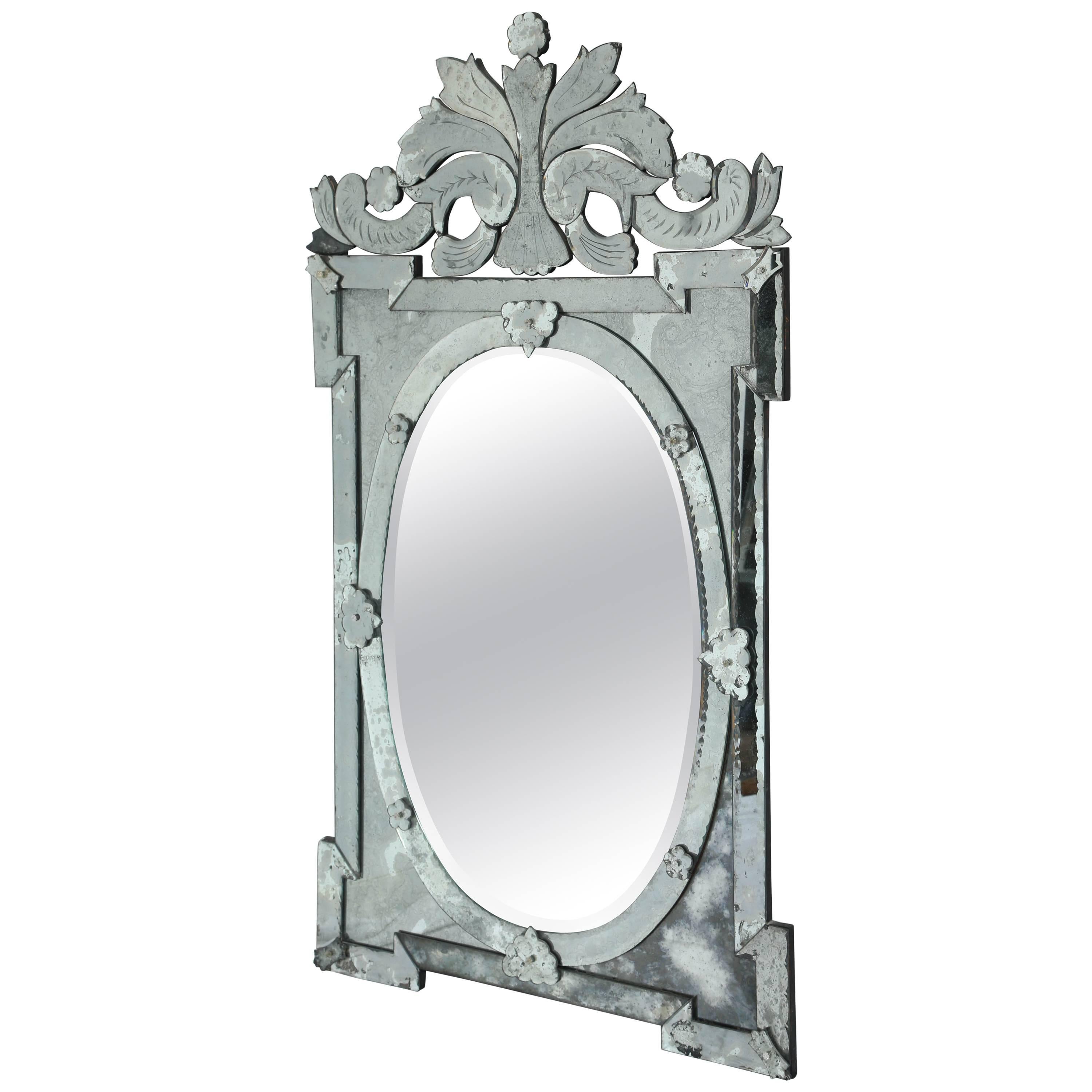 Exquisite large scale Venetian mirror with beautiful hand etched designs throughout. The mirror features a stunning oval centre within a shield shaped frame. Pediment top features ornate scrolled designs. Has antique glass borders in hues of smoked