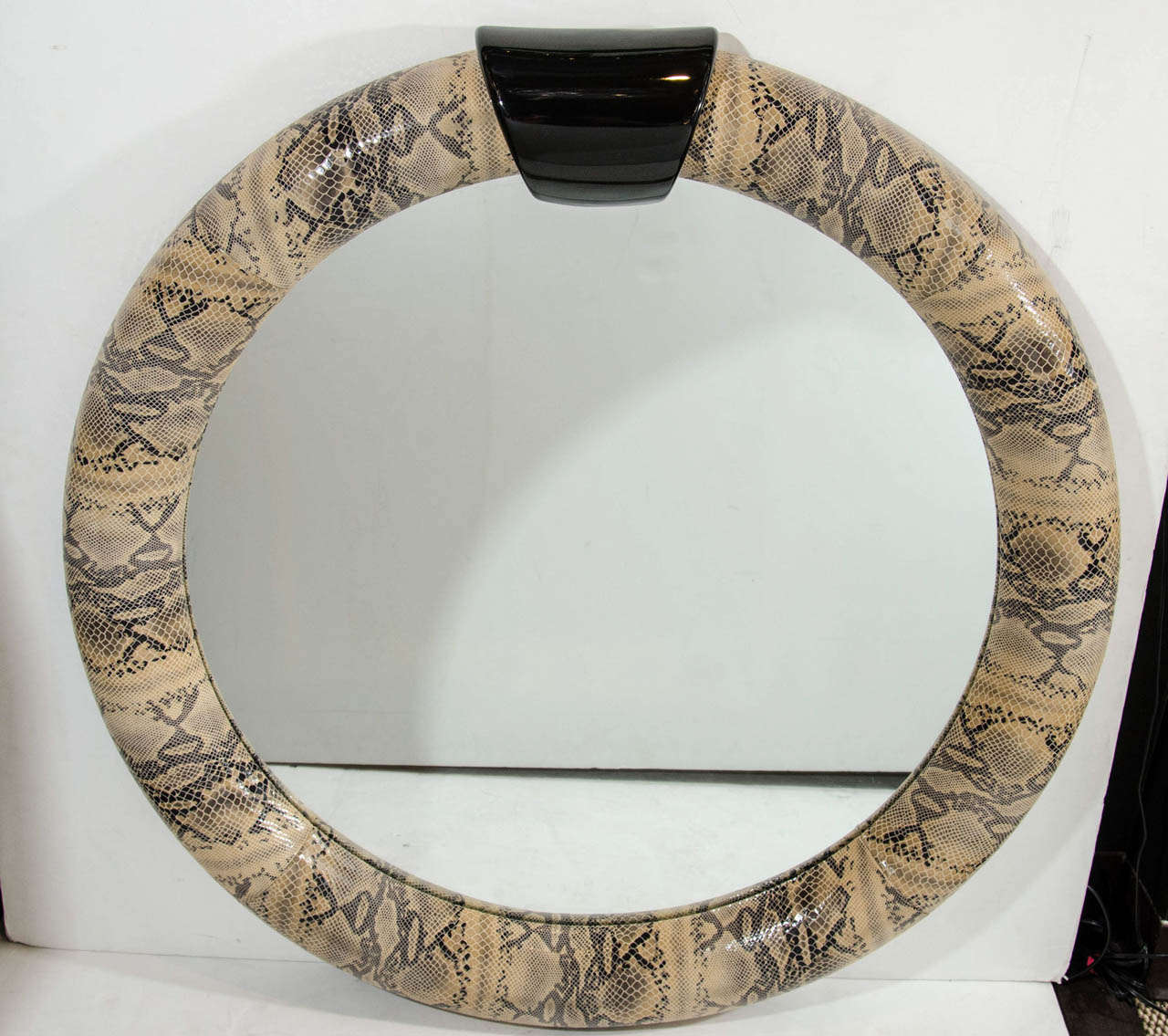 Mid-Century Modern round mirror wrapped in stunning embossed leather with snakeskin design. Python print leather with lacquered ebonized wood pediment top.
