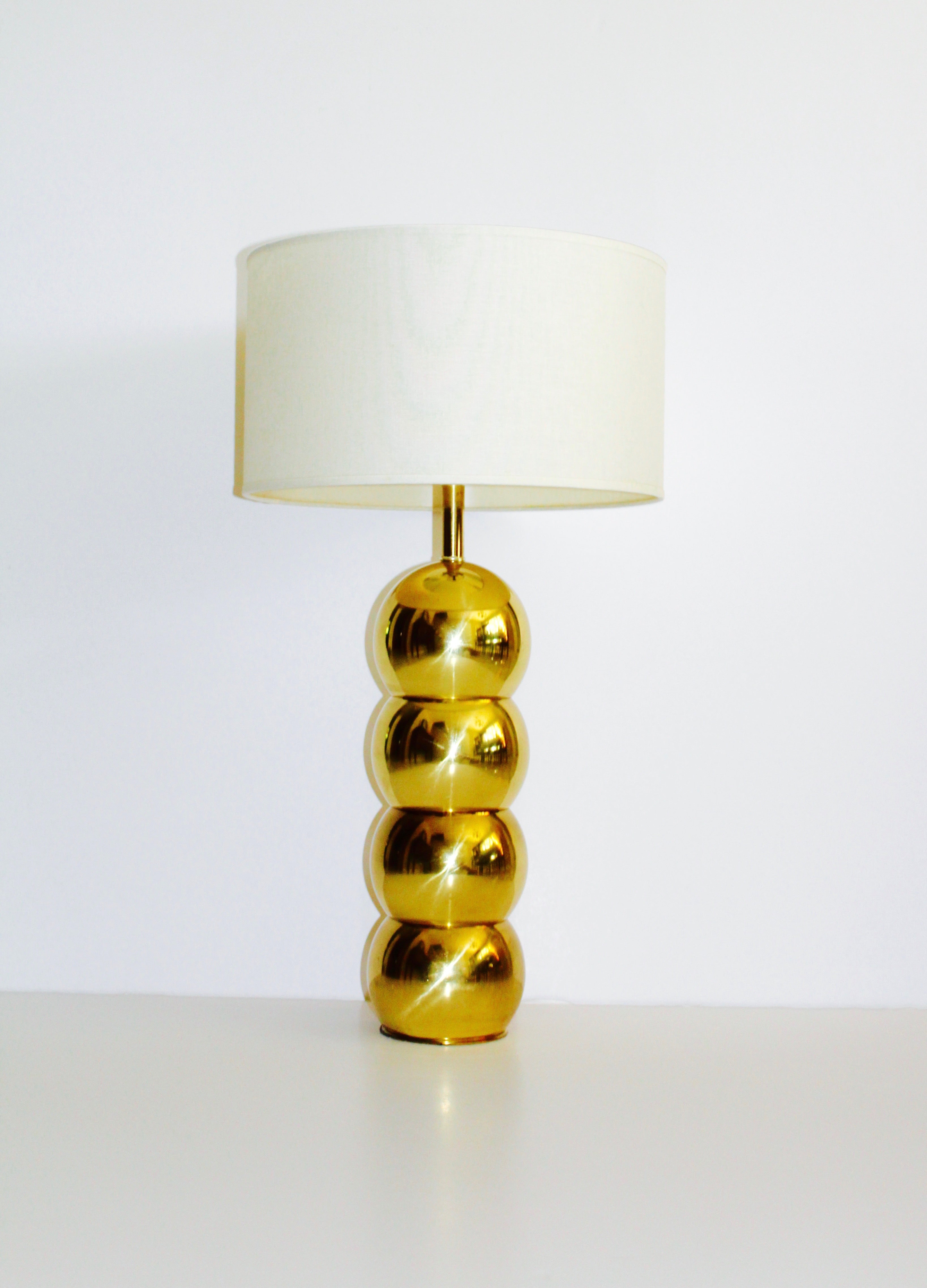Chic Mid-Century Modern brass metal lamp with Space Age design. Comprised of four stacked brass balls or globes with caterpillar form. Fitted with linen drum shade in off-white.