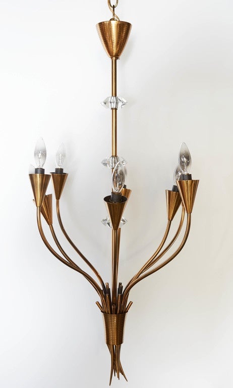 This spectacular pendant chandelier features eight outreaching arms in a tulip form. Chic and Minimalist, the frame has been finished in patinated brass. Three cut crystals ascend the central rod, with a cluster of stems or thorns punctuating lower