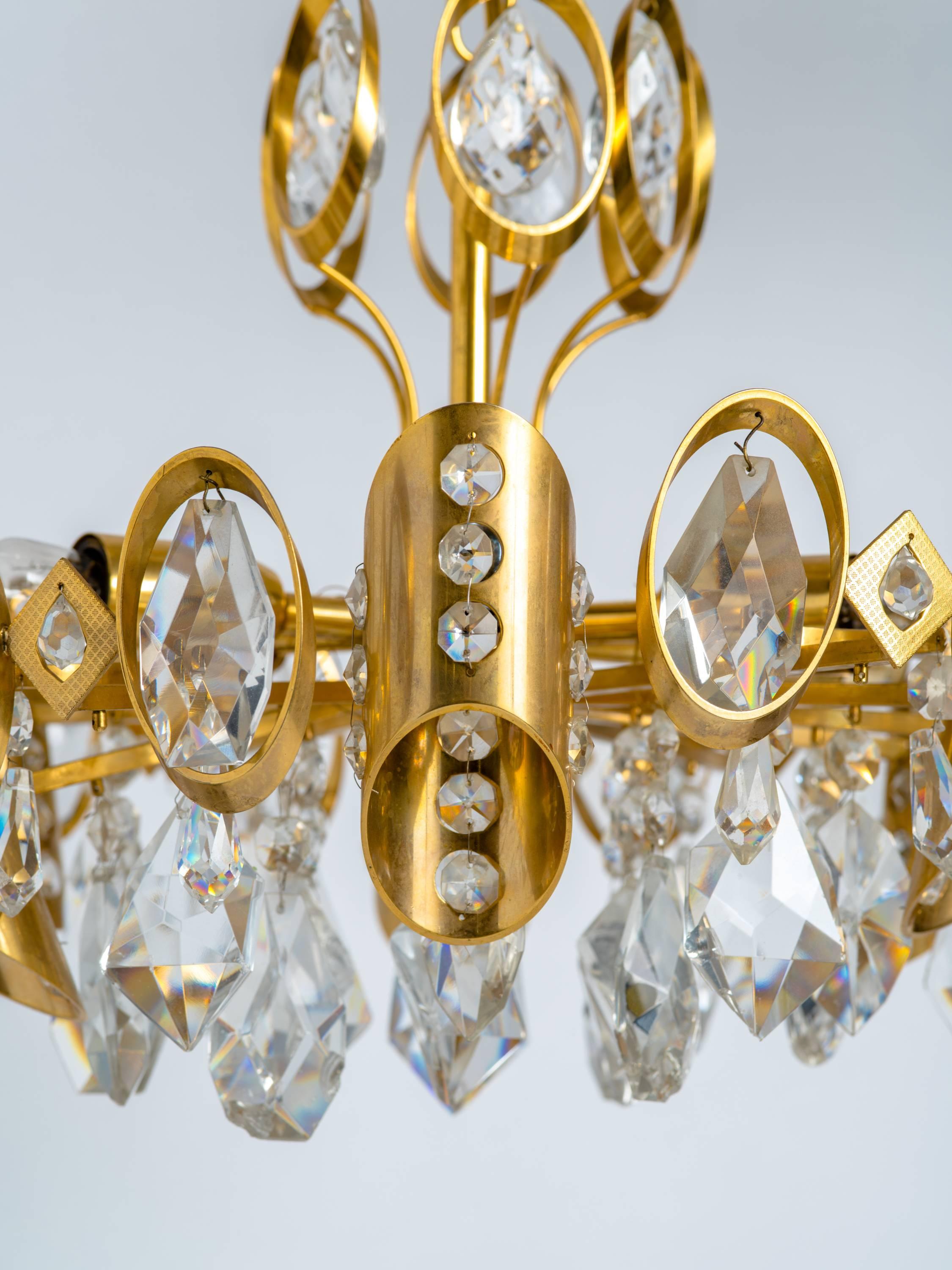 Stunning Mid-Century Modern chandelier with gilded brass frame and cut crystal pendants. Multiple tier design fitted with six radial lights and asymmetrical cylinders with beaded crystal accents.