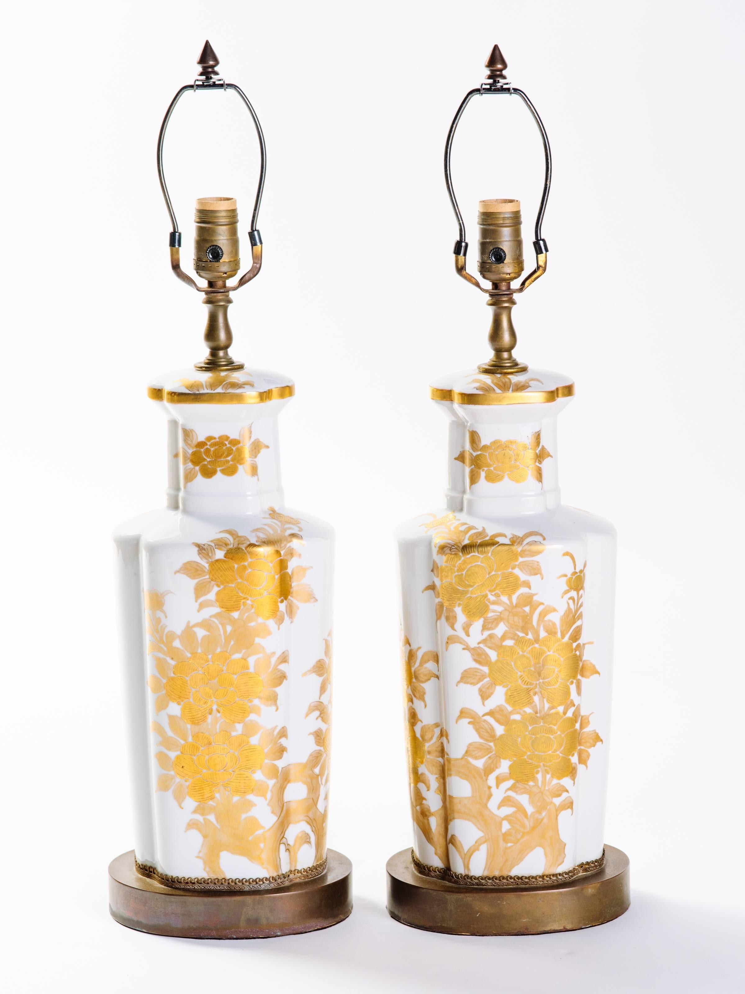 Pair of elegant Japanese porcelain lamps with hand-painted floral motif. Mid-Century lamps have white glaze finish with gold leaf designs, and hand-forged bronze base and fittings. Shown with custom narrow drum shade in silk.