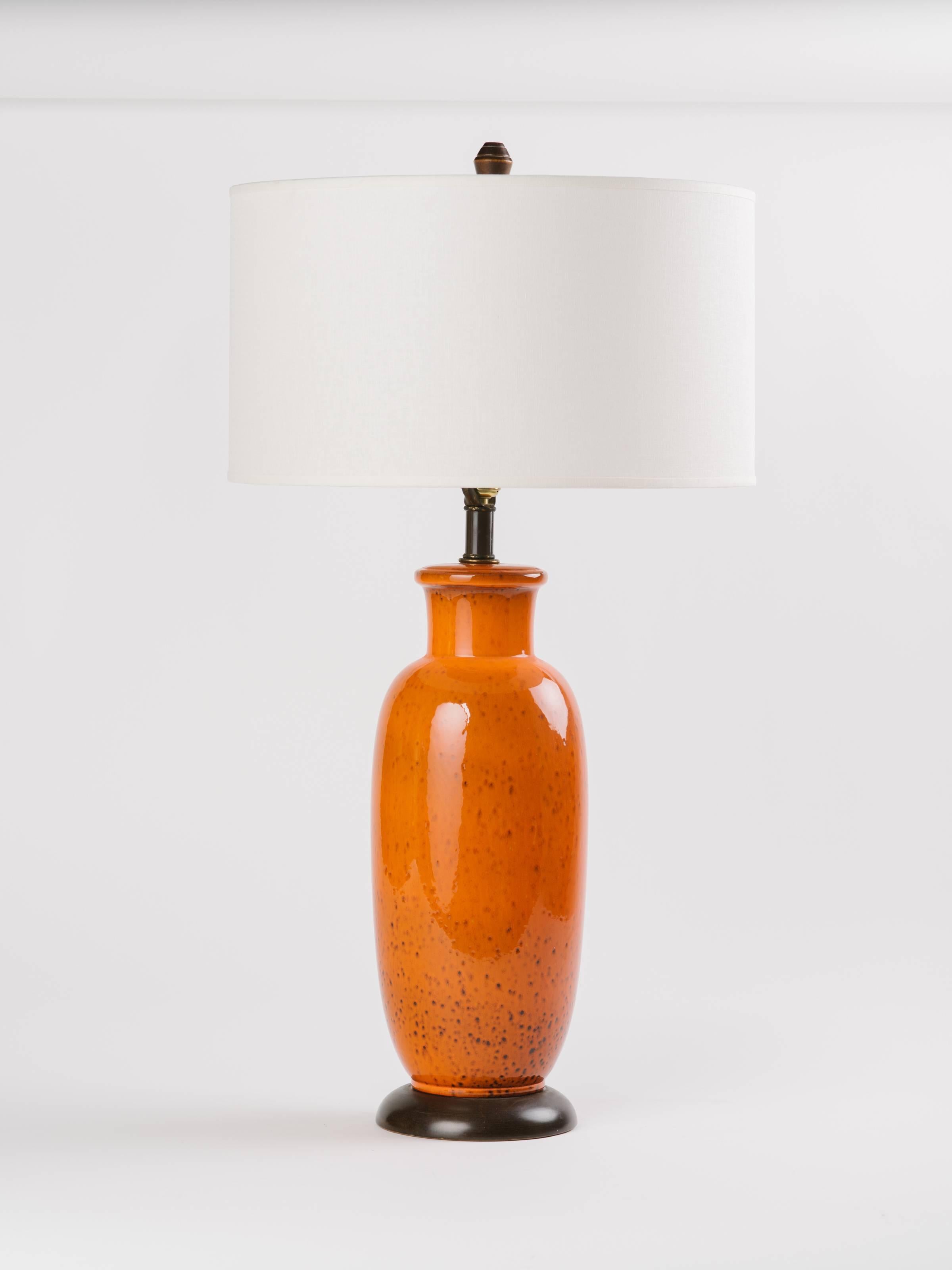 Pair of midcentury ceramic pottery lamps with glazed finish in vibrant burnt orange. Lamps have modern baluster forms with blackened dimples throughout. Walnut wood bases and shown with custom linen drum shades.