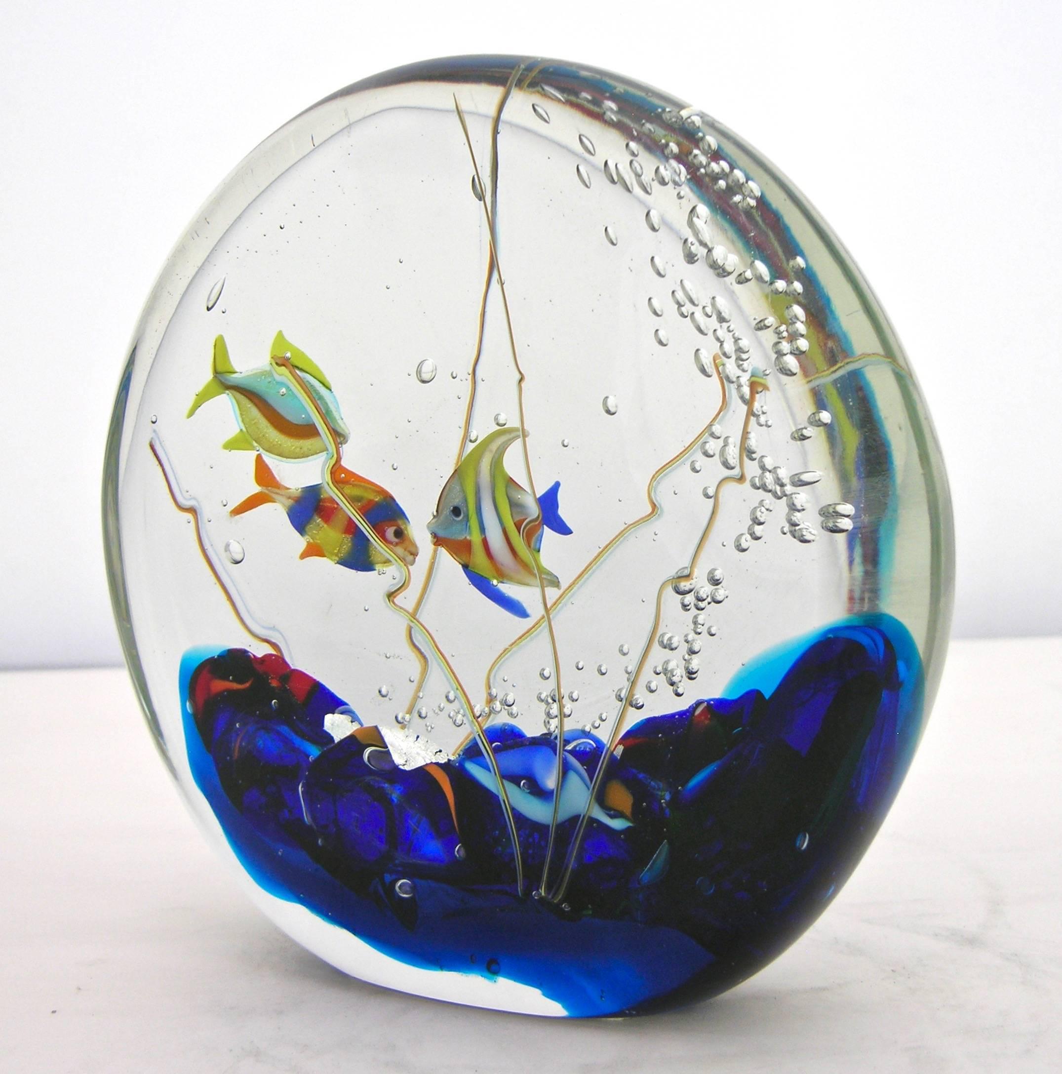 This aquarium sculpture in blown Murano glass is signed by Alberto Dona', of flat round shape, decorated with three tridimensional colorful fishes amongst bubbles rising from a blue sea bed highlighted with pure silver leaf. High quality of details