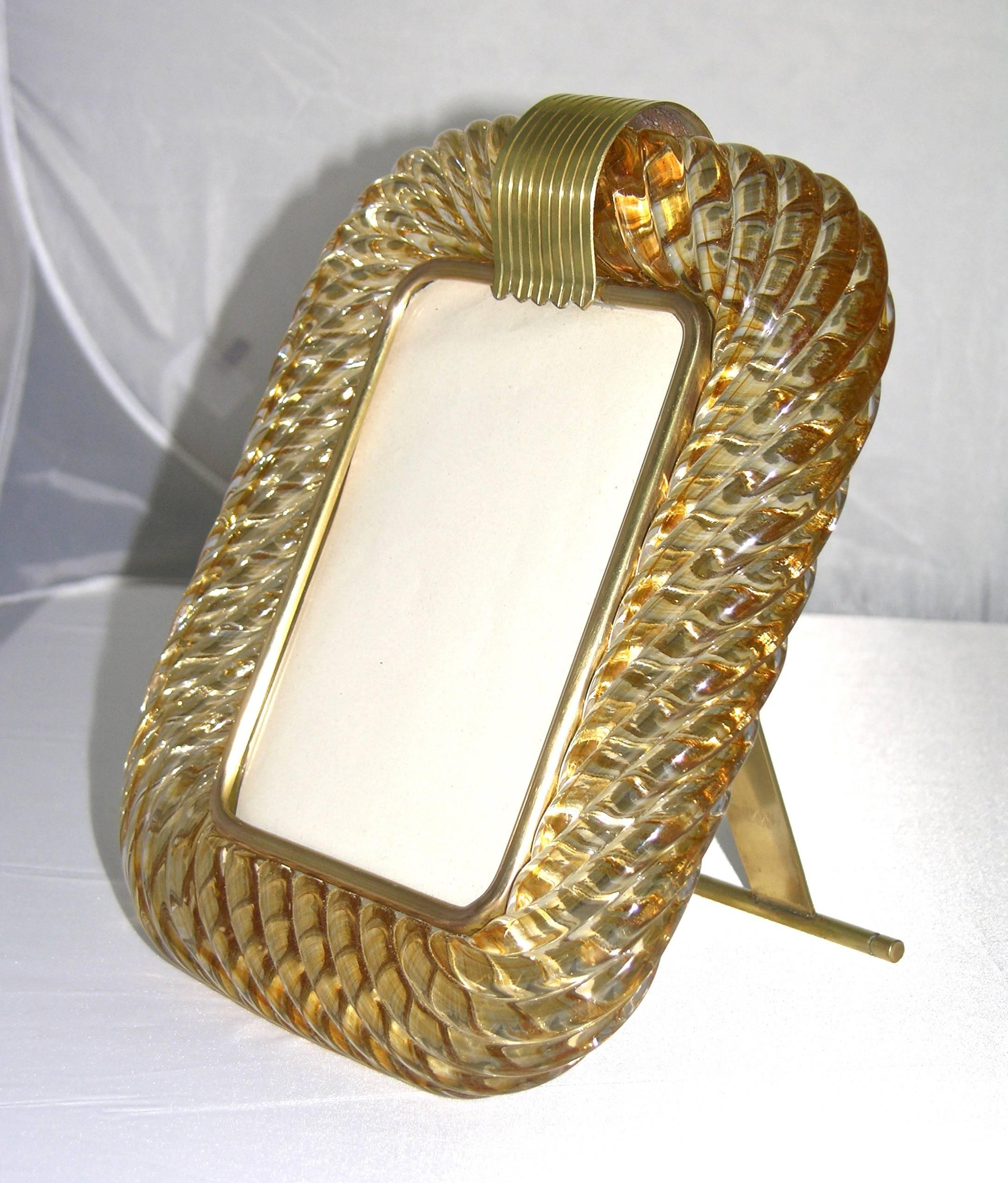 1970s amber gold Murano glass photo frame worked with “torchon”. Handcrafted twisted Murano glass blown with amber to give a golden glow throughout, enhanced by the reflections of the ribbed decor, on a handmade bronze support signed by Barovier