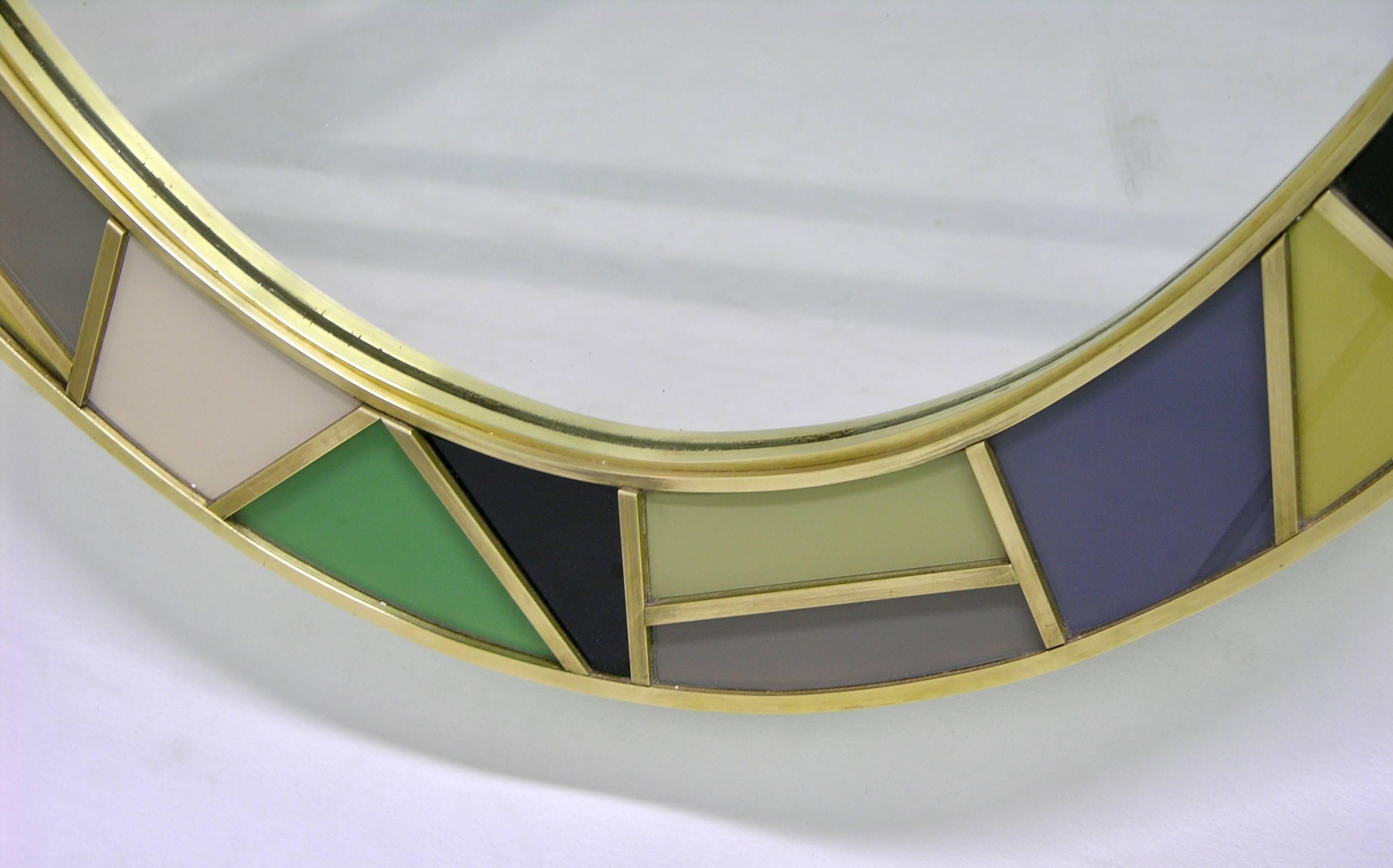 An Italian one-of-a-kind colorful oval mirror of grand size and modern design, entirely handmade. The central oval plate is framed by a double brass border that defines the substantial glass frame decorated with thick handcrafted brass insets that