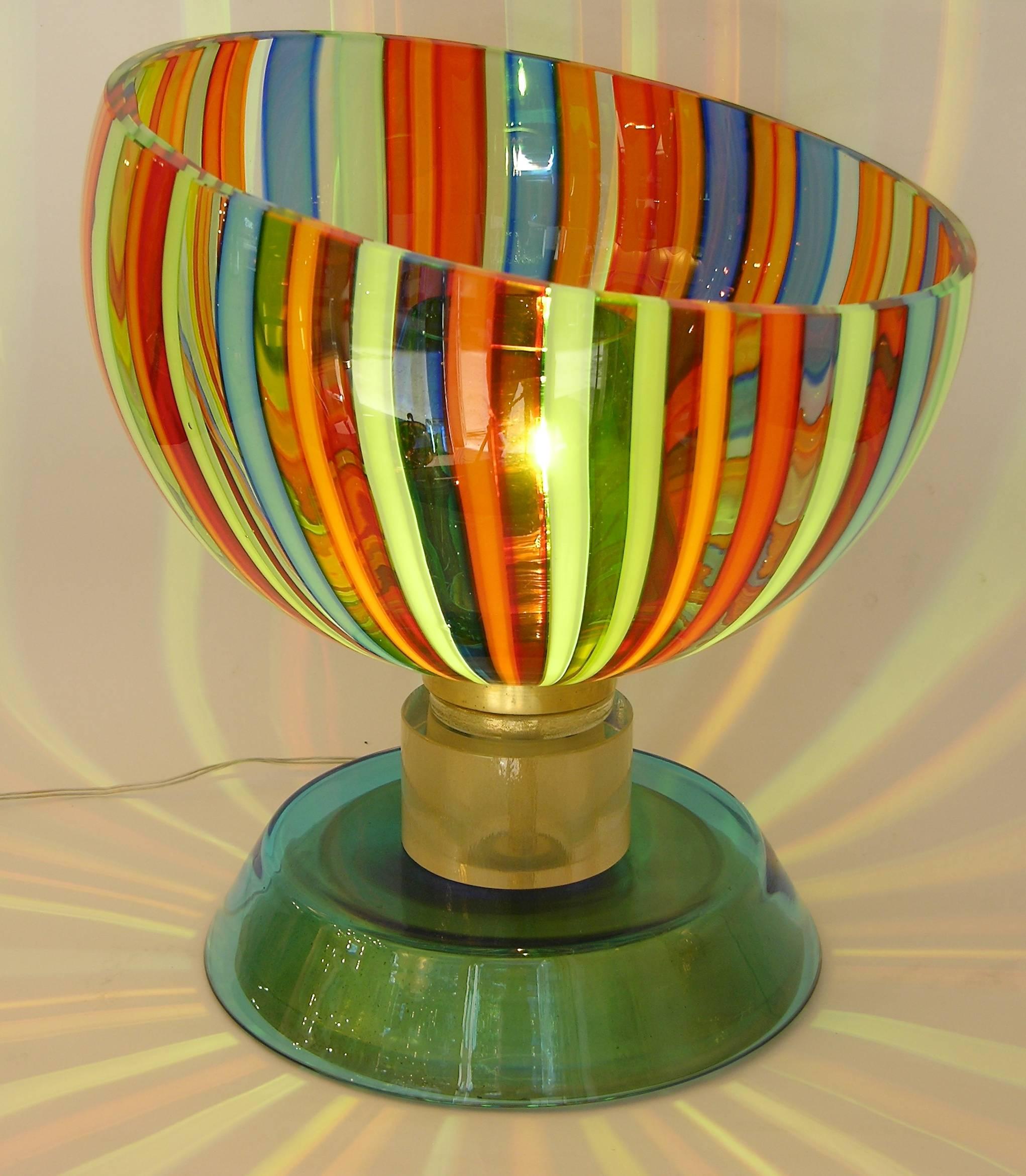 A colorful pair of blown Murano glass lamps by Cenedese, the rainbow stripes bowls with a unique diagonal shape contain a green glass shade and project atmospheric shadows when lit, raised on a round manufactured bronze base covered in aqua blue