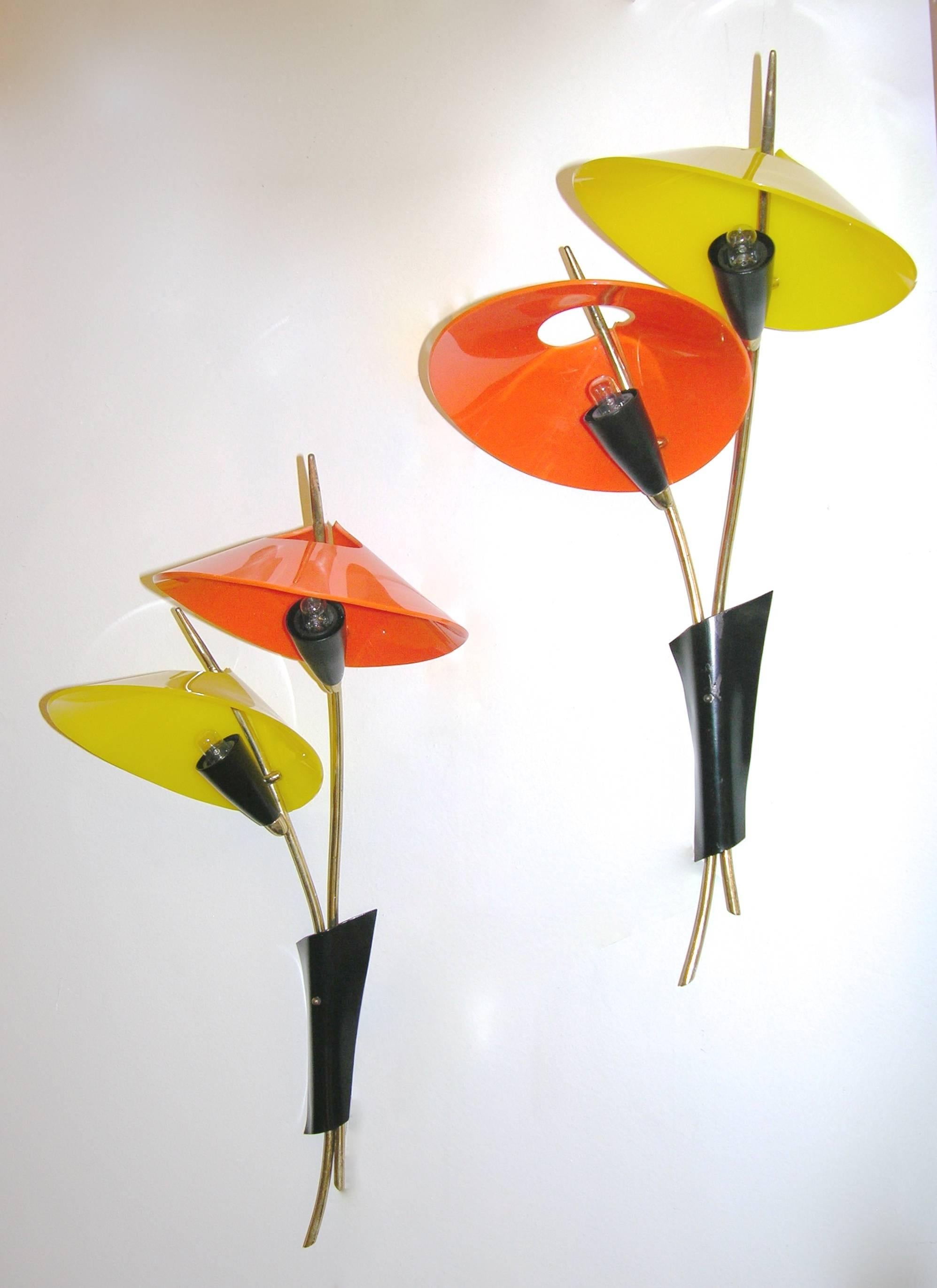 A fun pair of wall lights, Italian manufacture, in the shape of two oriental parasols, one in orange and one in yellow Perspex, on bronze stems bunched in an asymmetrical black metal support. In original condition.