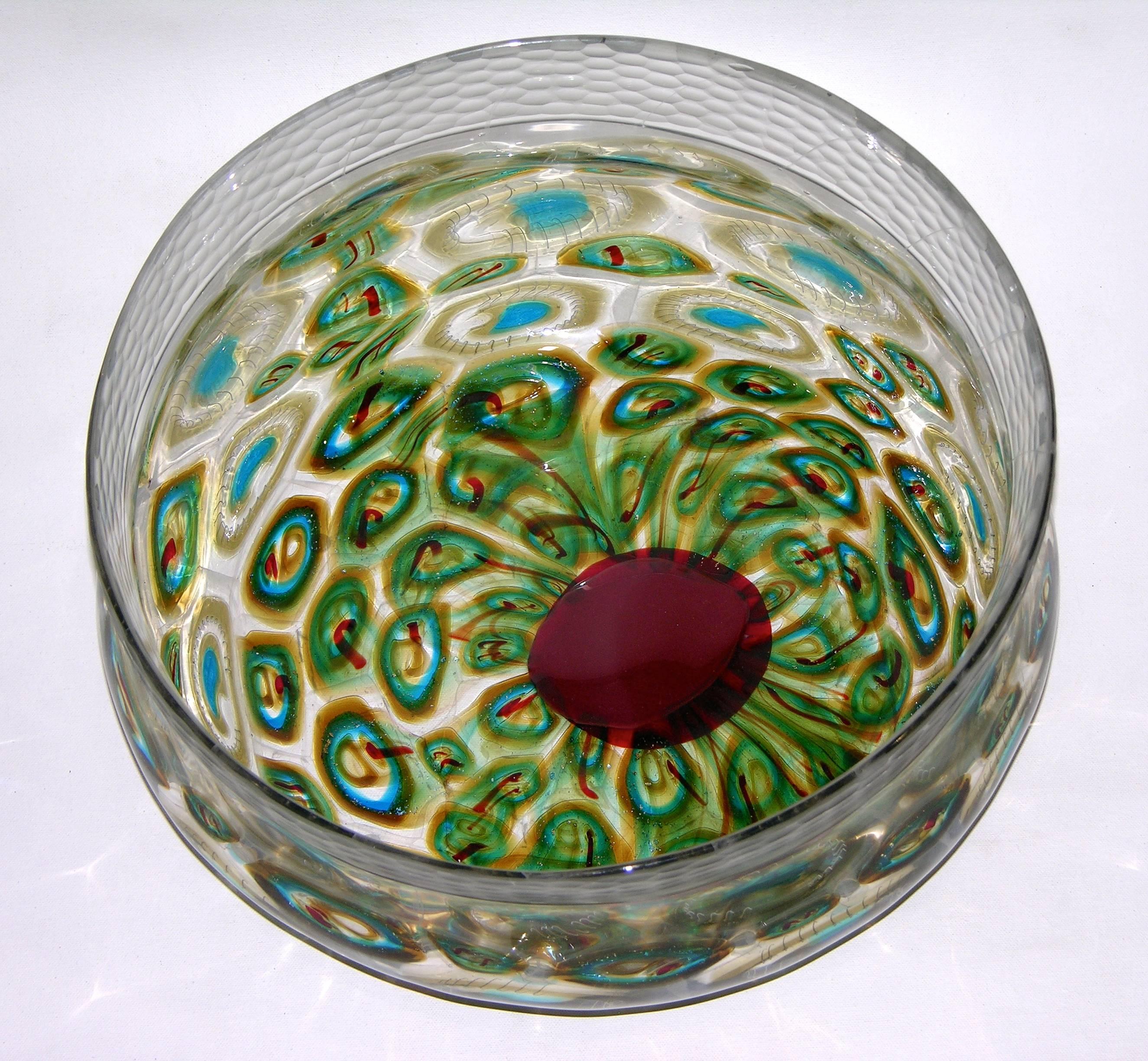 A work of art by Afro Celotto, a sophisticated creation in the shape of a bowl in blown clear Murano glass preciously worked, like the plumage of peacock, with green, aqua blue and red murrine highlighted with white fili and enhanced with inclusions