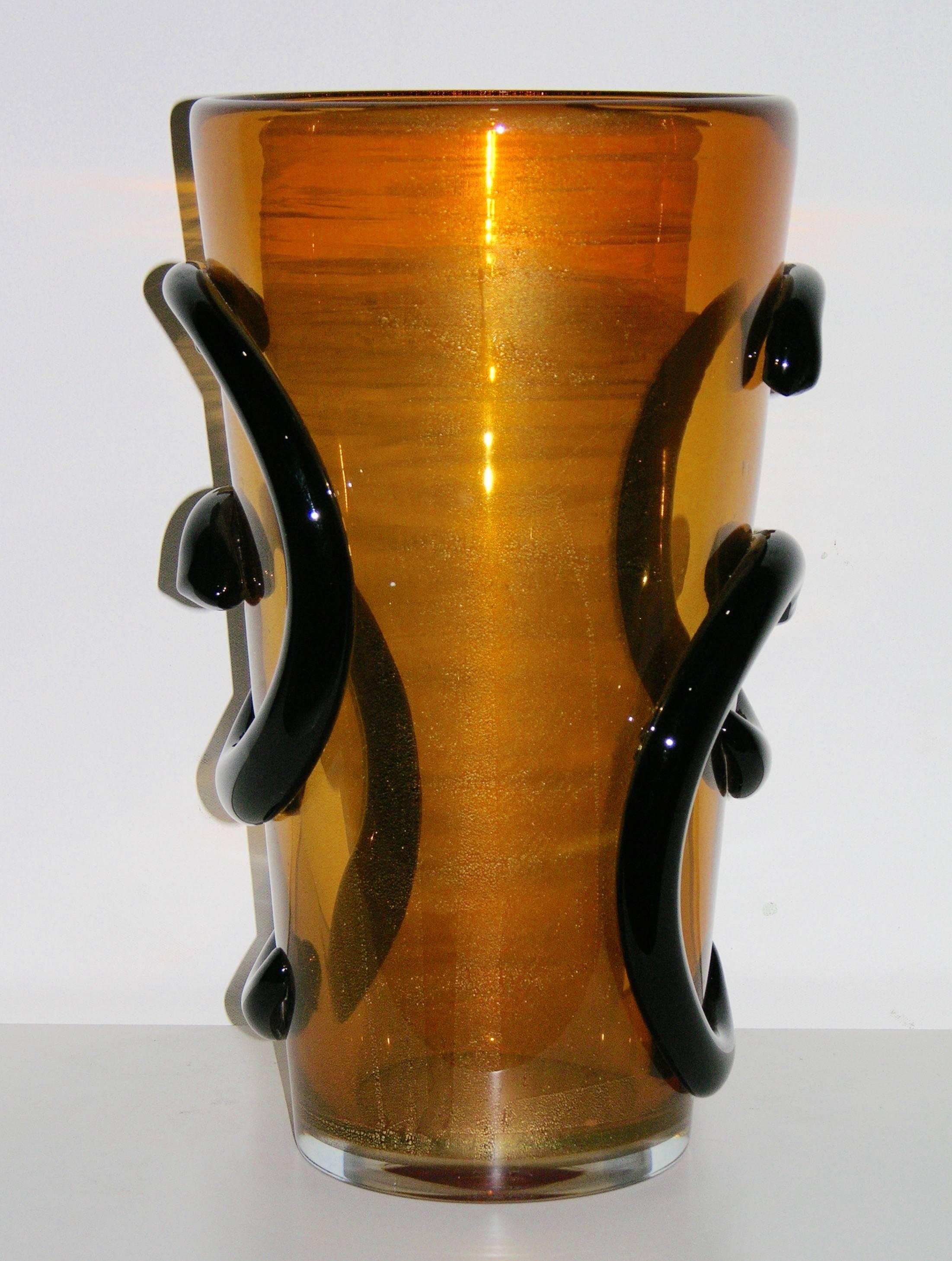 1980s, elegant pair of vases in amber blown Murano glass with pure 24-karat gold worked through that creates a fired shimmering finish and glow. 
The color is striking and highlighted with “C” black glass scrolls in relief, adding uniqueness and