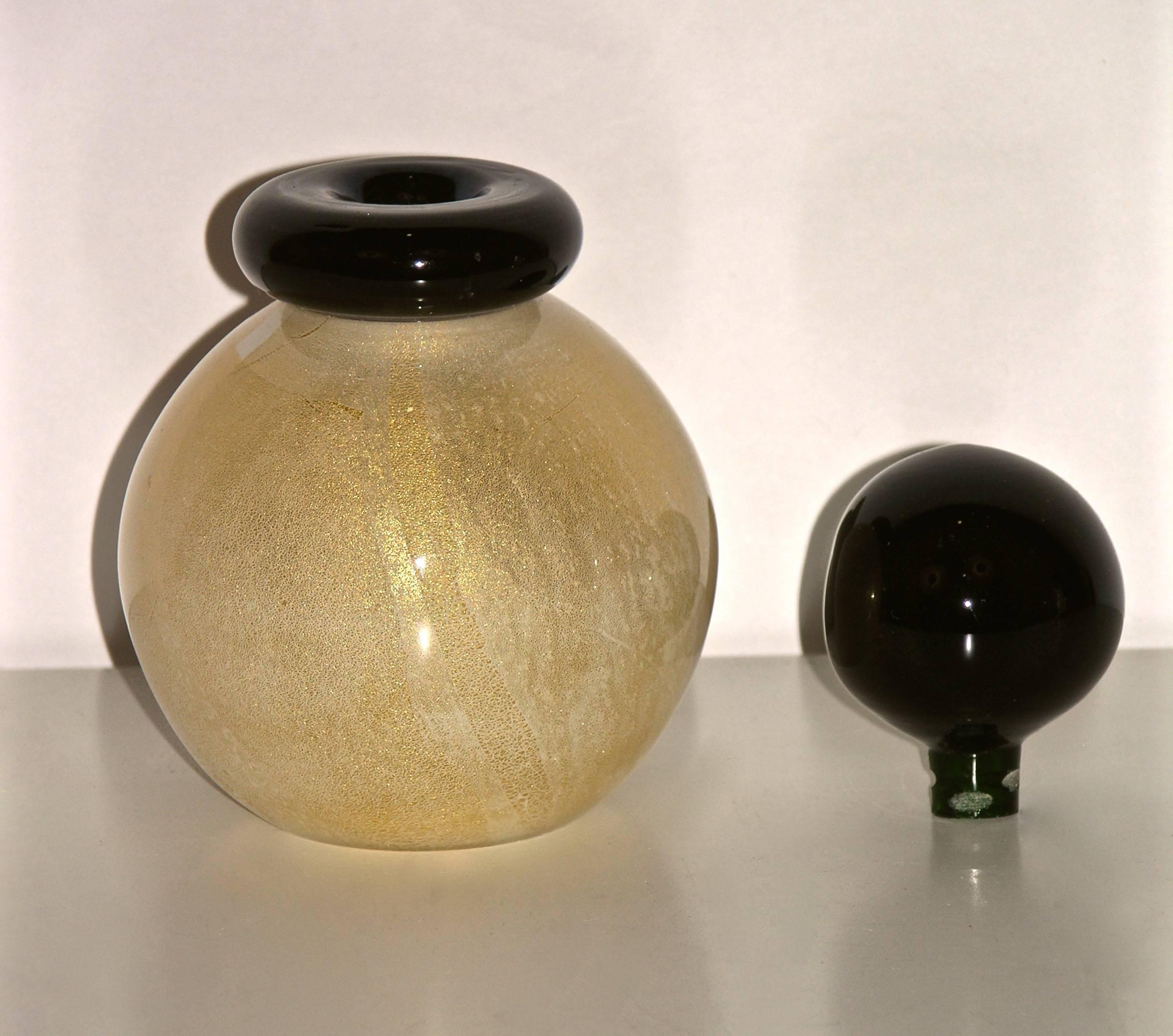 1970s Murano glass bottle by Archimede Seguso, signed. The round body is worked with pure gold leaf in the overlaid glass, cleverly accented by a lipped neck in bottle green glass accompanied by its original stopper in the same bottle green color.