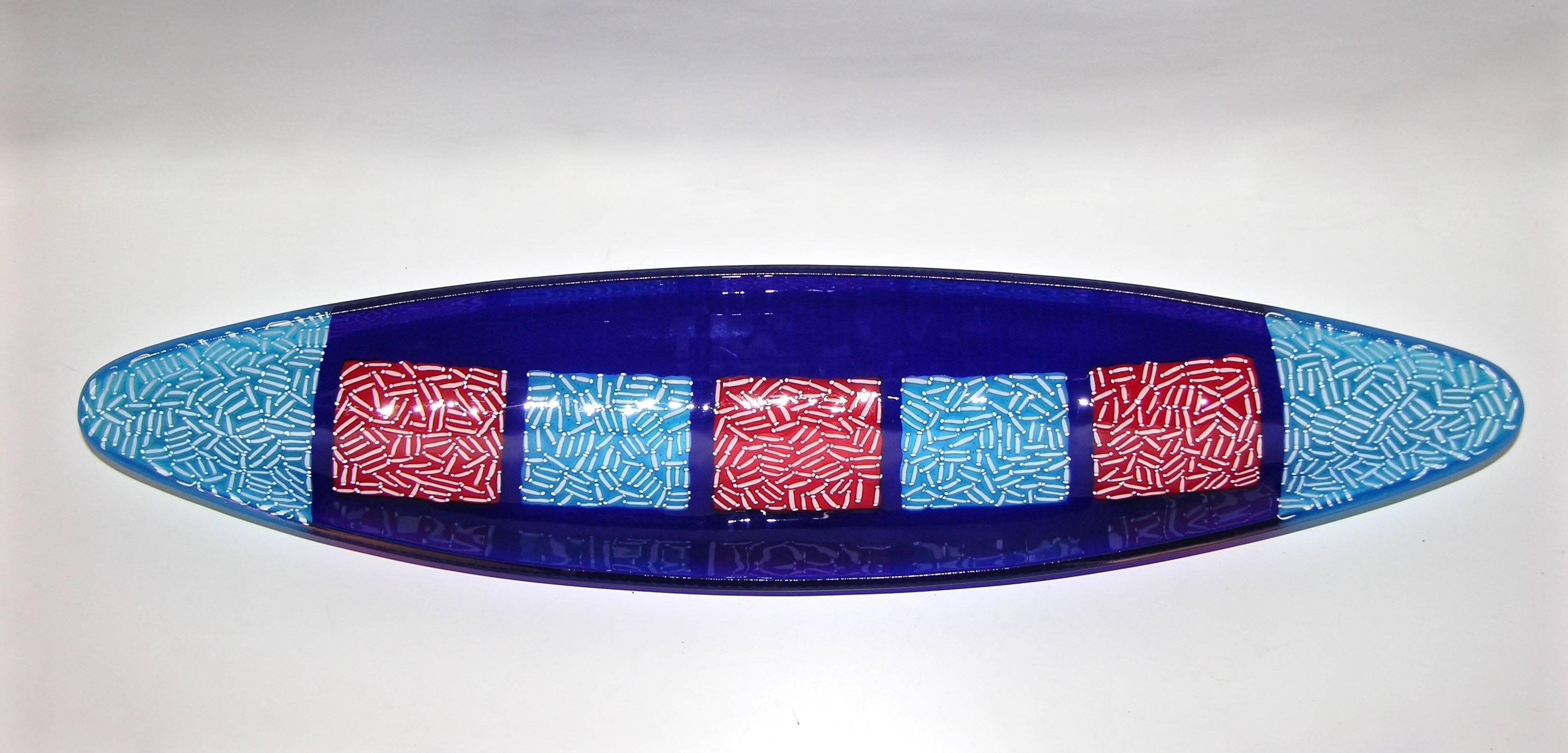 A contemporary bowl of elongated shape like a gondola, in Murano glass, with a decor like a mosaic giving an orientalist flair, created with the highest quality craftsmanship using the fusion technique, exclusive for Cosulich Interiors. The enamel