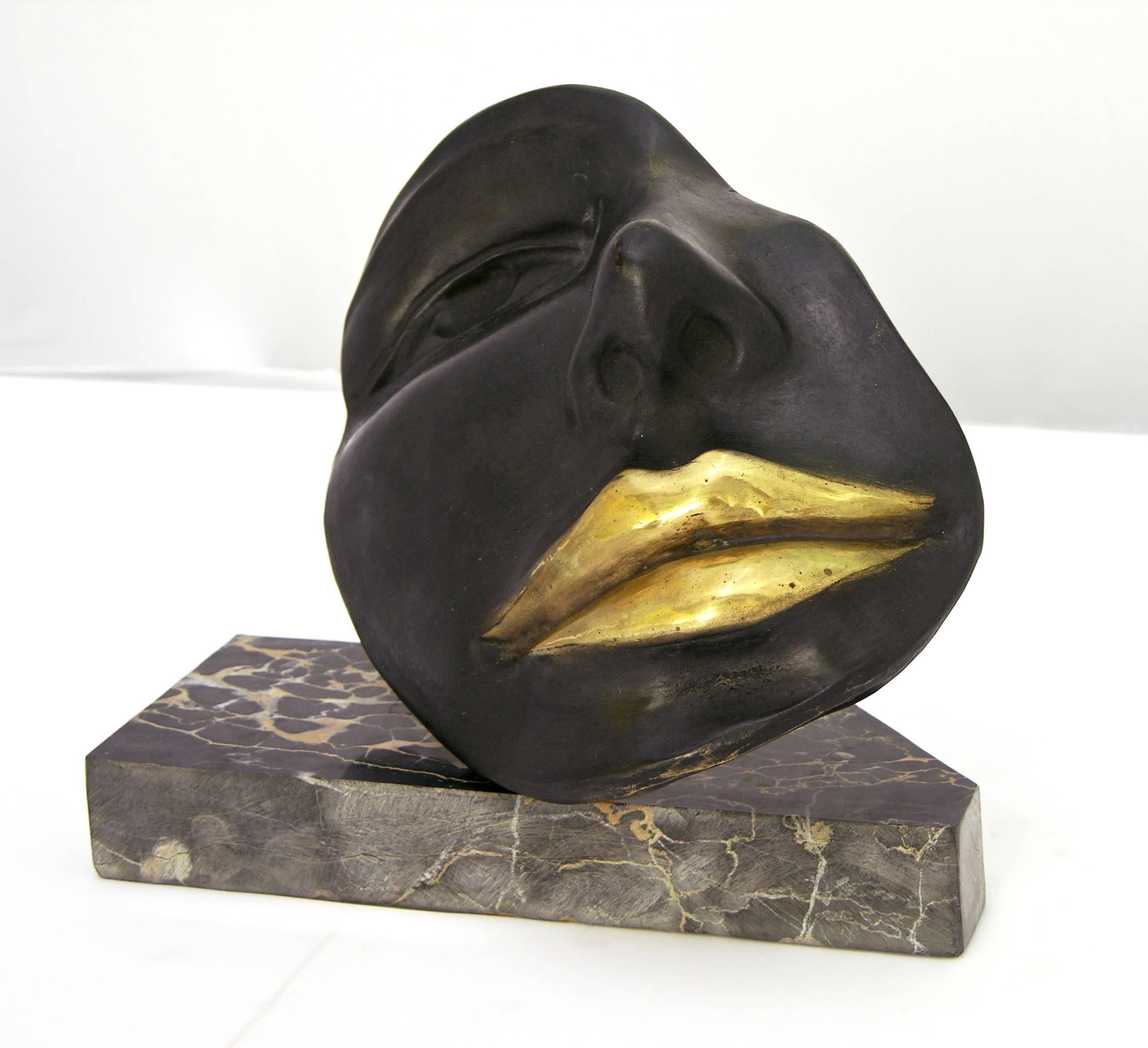 A sexy contemporary cast bronze of a partial feminine face accented by hand gilt lips, resting on a variegated black and white Italian marble base with attractive trapezoid shape by the Italian artist Ginestroni, signed piece. 
Ginestroni, a