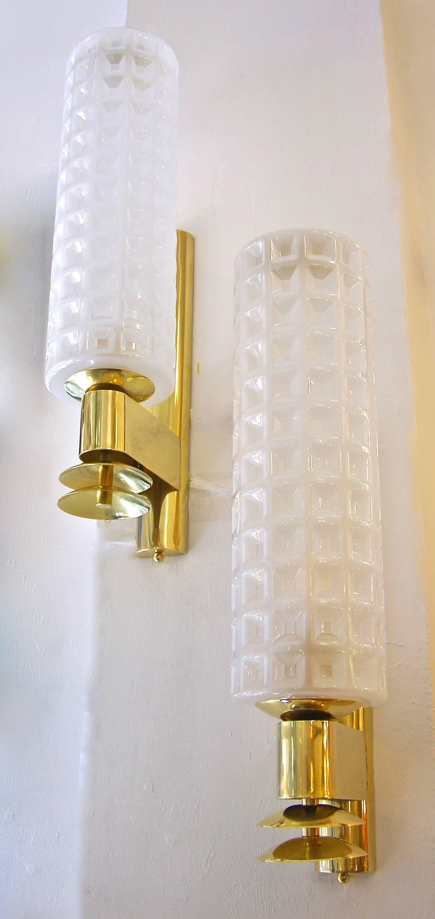 1980s Italian sophisticated cylindrical sconces of Art Deco Design, in milk white blown Murano glass, handcrafted with a textured geometric waffled pattern, on a handmade brass support. High quality of execution and gold brass finish with elegant