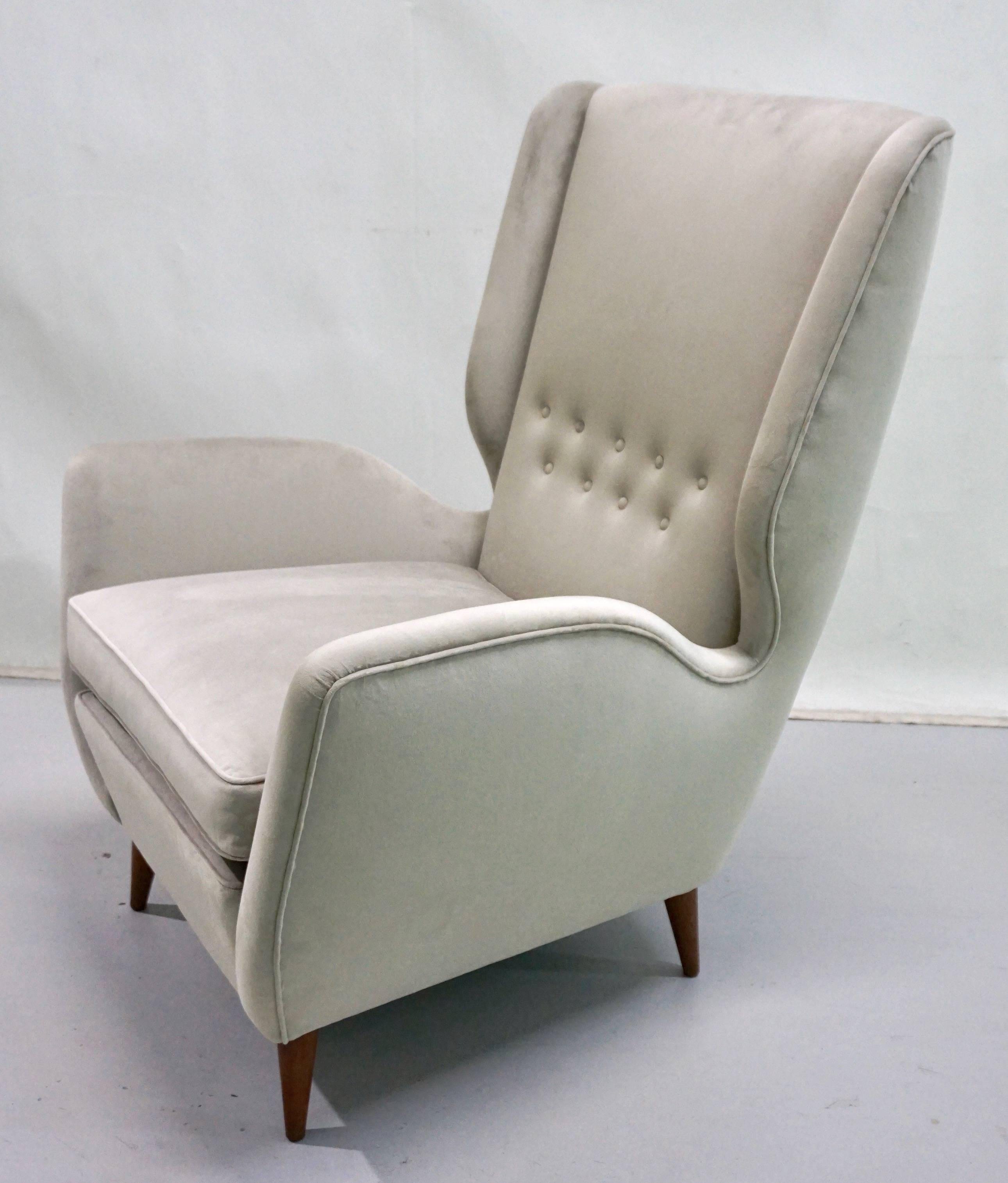 These very comfortable high back armchairs by Gio Ponti, a statement of elegance and modern Italian Design, have very clean cut aerodynamic lines with very chic indented sides and slightly folded button-tufted back, raised on walnut legs. They are