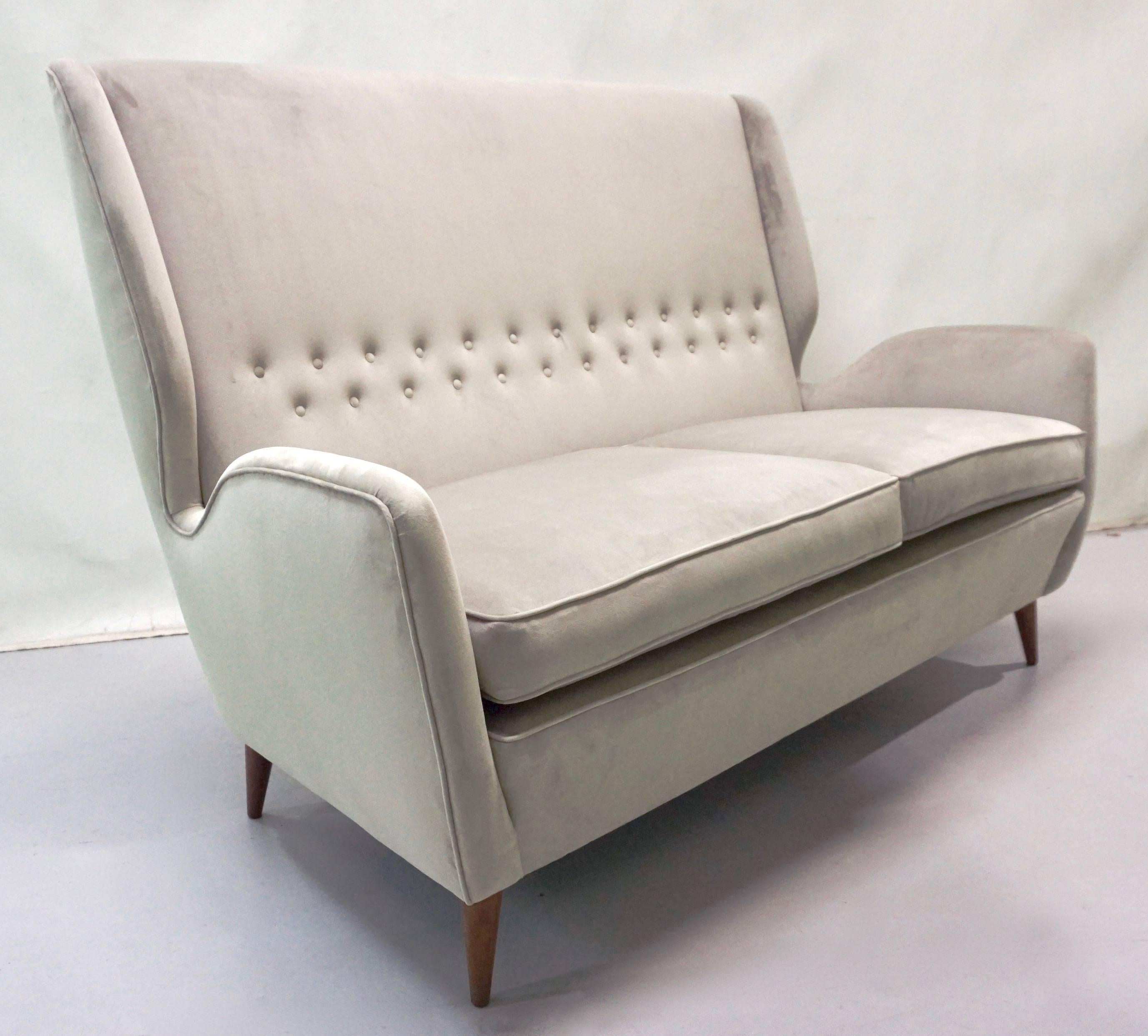This comfortable settee by Gio Ponti, a statement of elegance and modern Italian design, has very clean cut aerodynamic lines with very chic indented sides and slightly folded button-tufted back, raised on walnut legs. It is upholstered in light