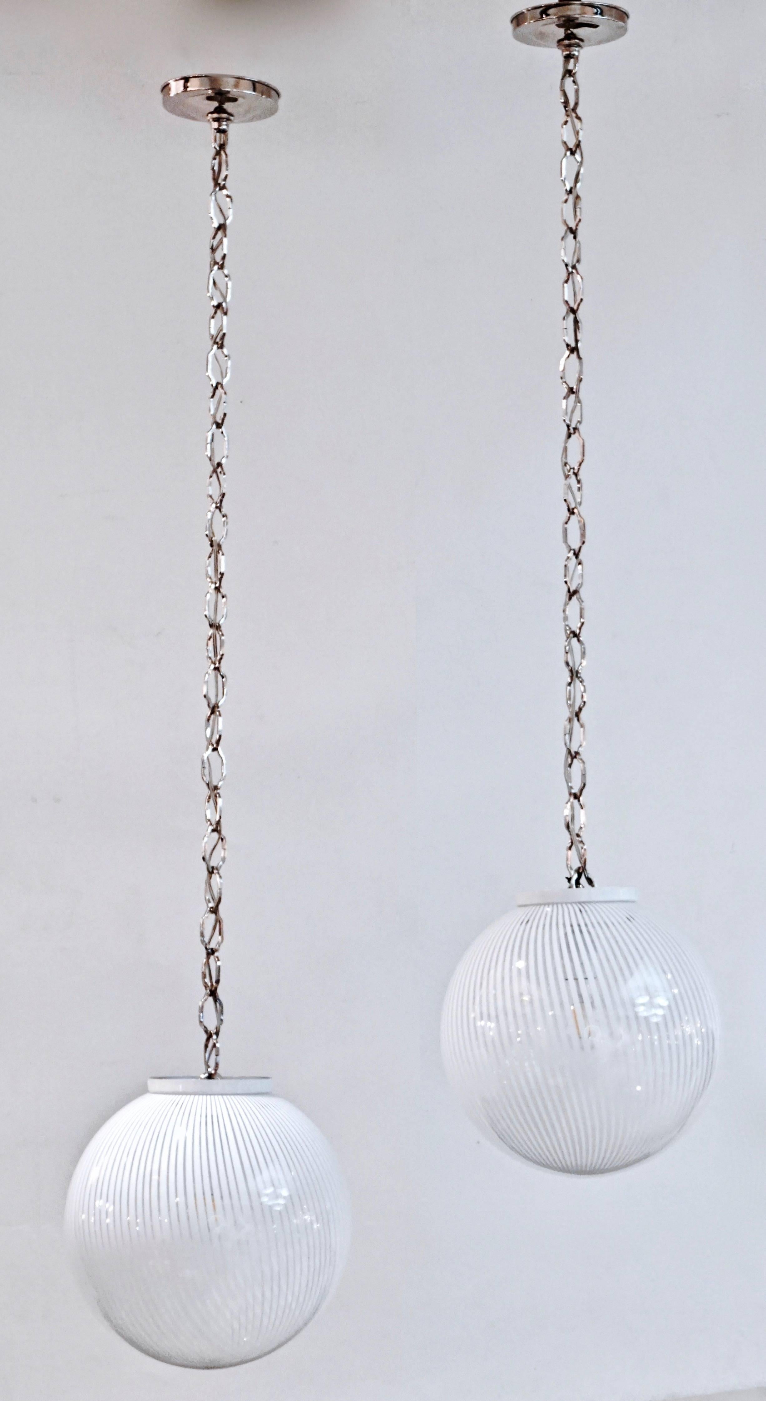 A pair of 1970s Venetian organic globe pendants by Ludovico Diaz de Santillana blown by Venini, in Minimalist clear Murano glass worked with perfect white filigrana, finished with a white lacquered metal round cover, hanging on a nickel chain with