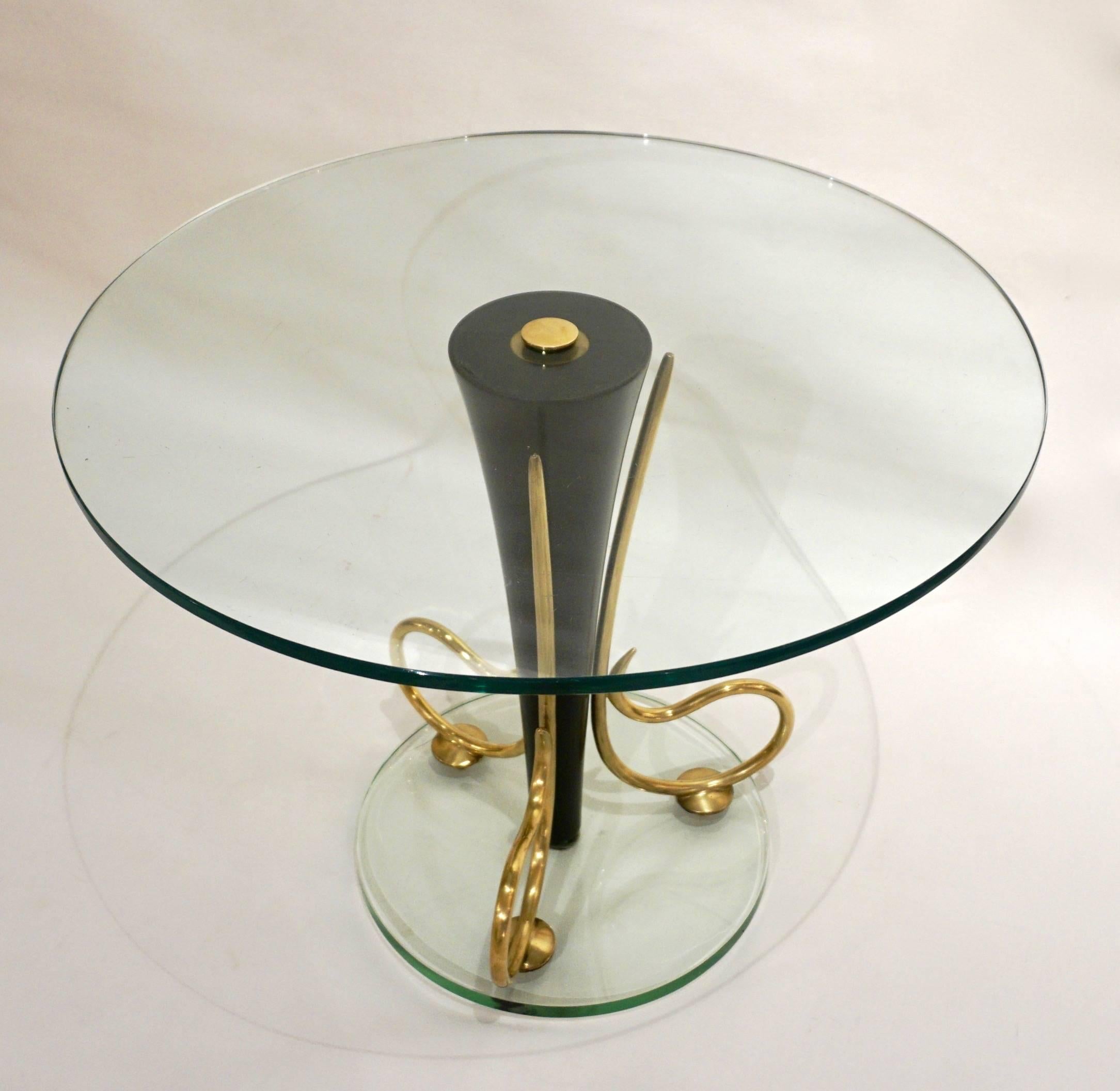 1950s elegant Italian coffee table entirely handcrafted with high quality of execution. The conical central support, in black lacquered metal, is adorned with three sophisticated brass scrolled side decorations on a glass base, raised on three brass