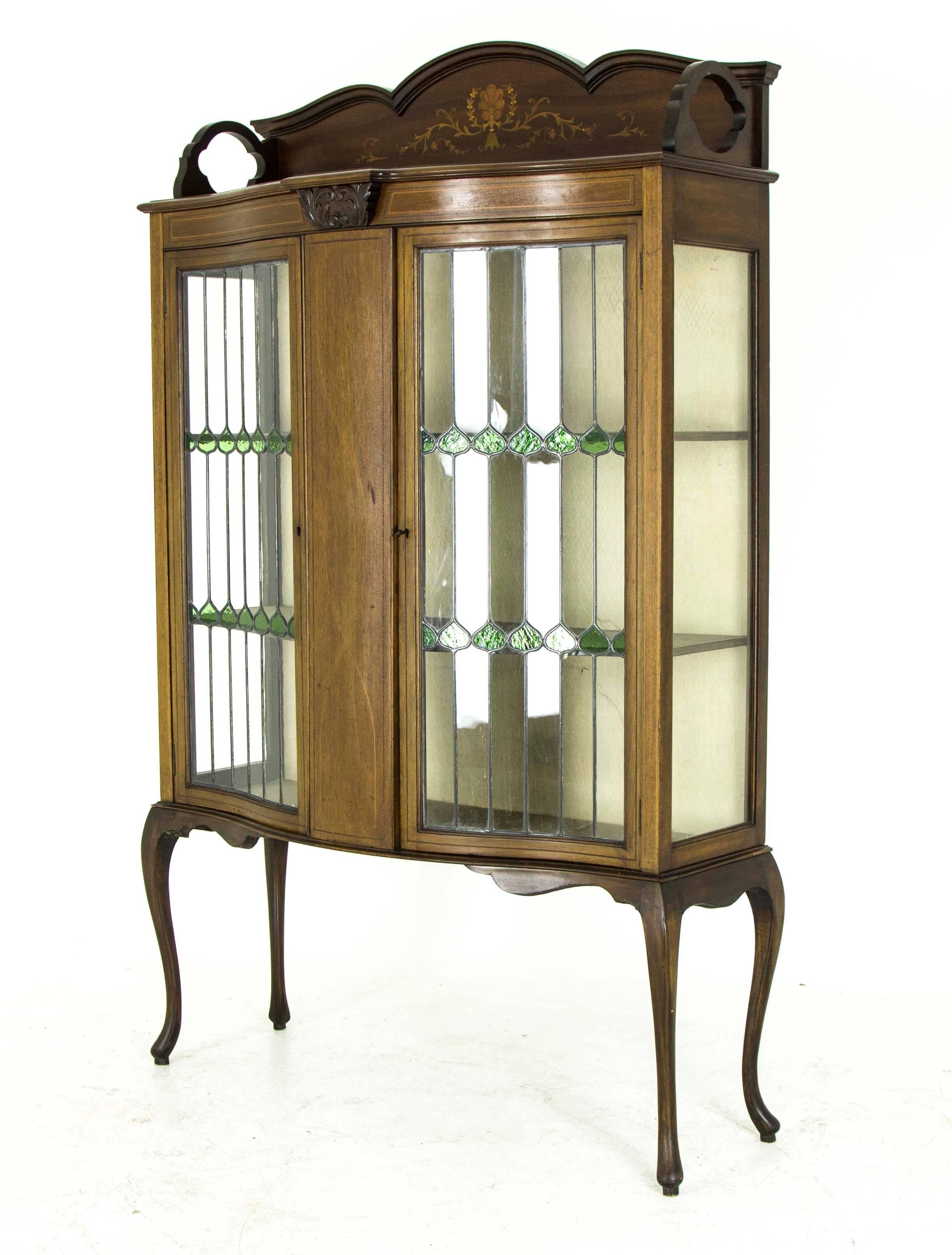 Scotland
1910
All original finish
Three quarter inlaid gallery above
serpentine front with central inlaid panel
flanked by a pair of stained glass doors
with two fixed shelves inside
fabric back and fabric shelves
fnding on very tall, shaped