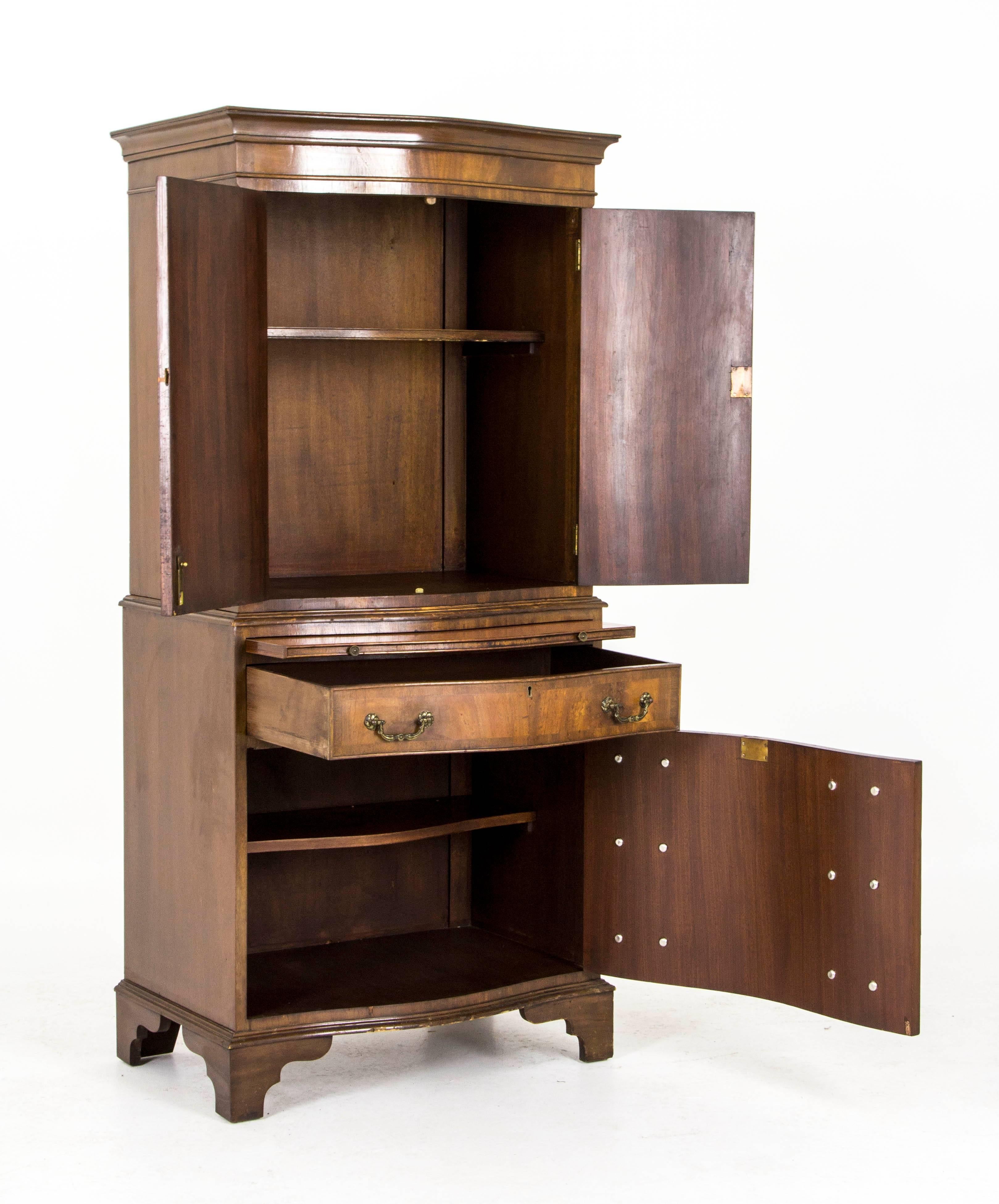 Scotland
1940
Original finish
Serpentine front doors enclose single shelf
Slide out glass shelf
Single drawer below
Concealed cupboard with false drawers
Single shelf below
Ending on bracket feet
Separates into two pieces
Some minor wear on front