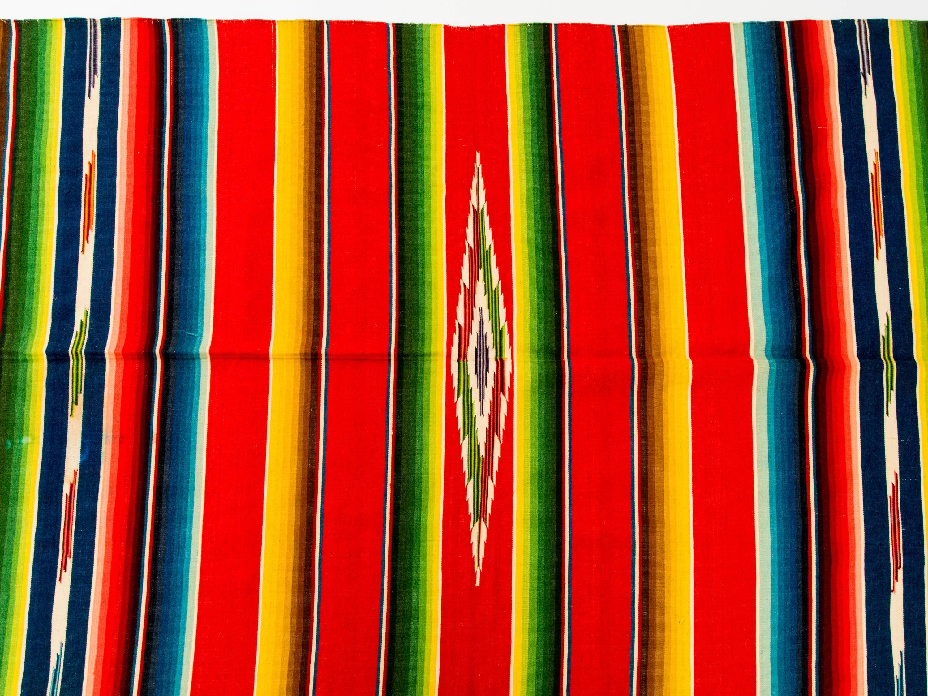 Vintage 1940s Mexican Saltillo serape blanket with multi-color stripe on red background. Serape has fine wool warp, and cotton fringe and weft.