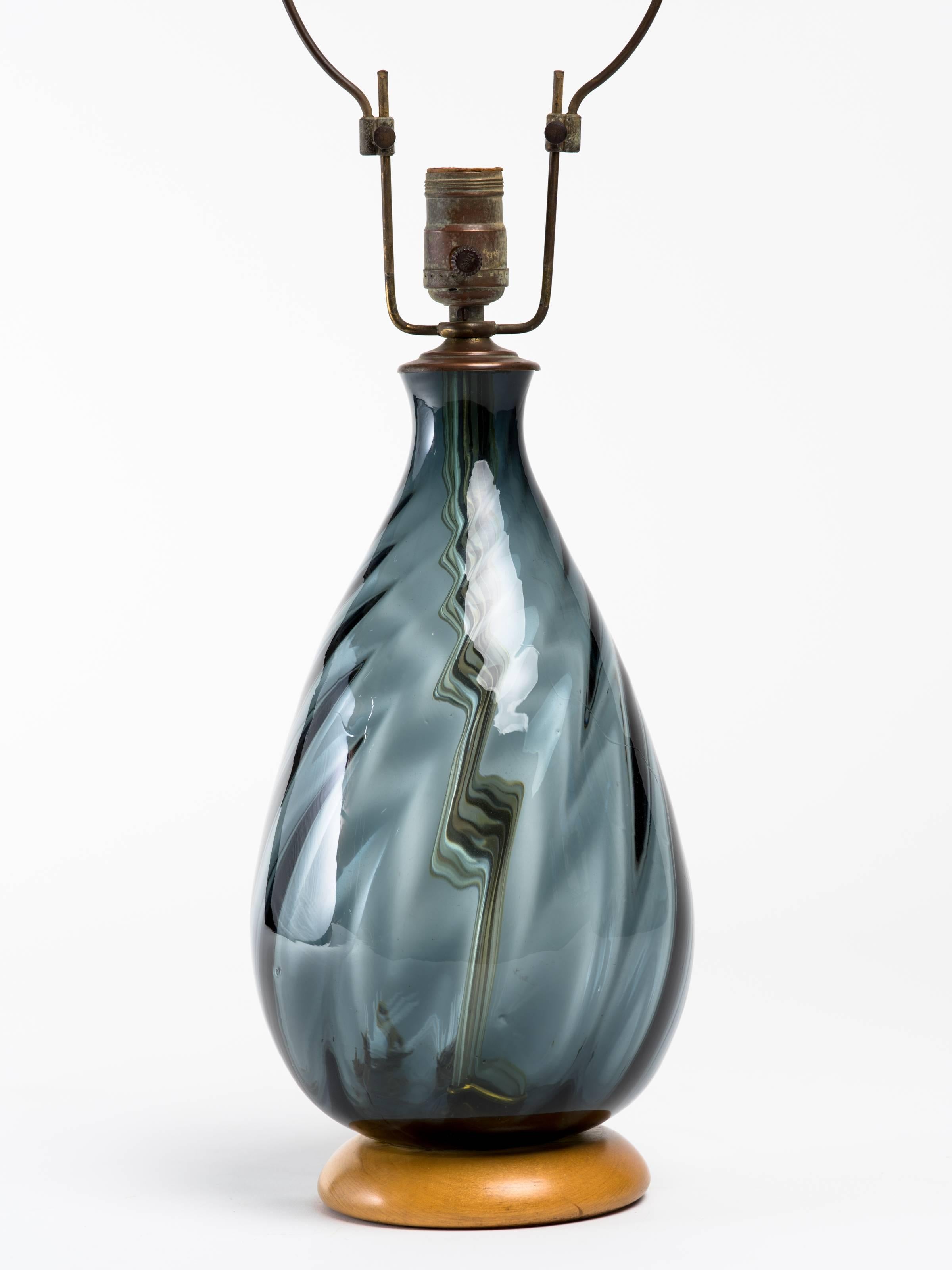 Lampe en verre bleu fumée Blenko avec base circulaire en bois. La quincaillerie et l'embout sont d'origine. La hauteur totale mesure 27 pouces, le corps de la lampe, 14 pouces de hauteur.
Signé avec une étiquette en papier sur la harpe, et