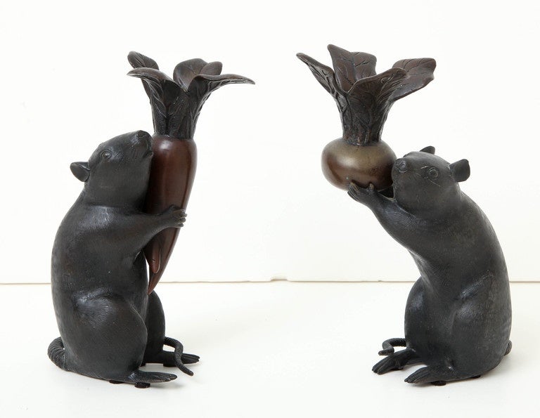 A pair of late 19th century Japanese bronze candlesticks modelled as crouching rats holding root vegetables