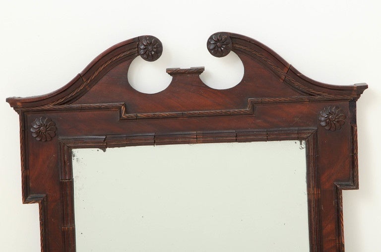 An 18th century English mahogany mirror with architectural broken pediment, carved rosettes, checkered banding and old glass plate