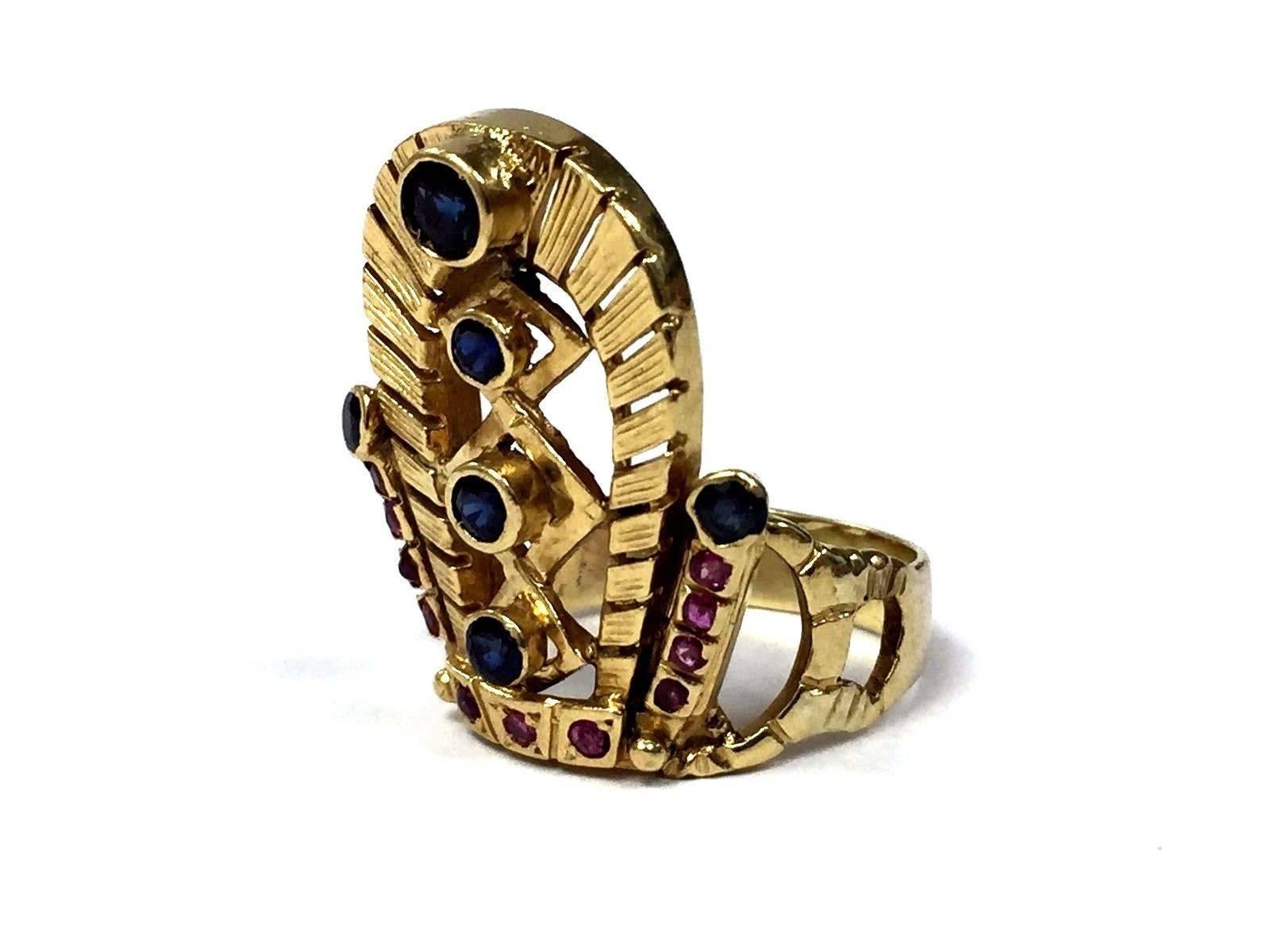This unique ring depicts an Egyptian Pharaohs headdress crown and features blue sapphires and rubies set in solid 18-karat gold. The ring shank is solid 14-karat gold. Truly a beautiful and special ring in person.

Gemstones: Six round sapphires =