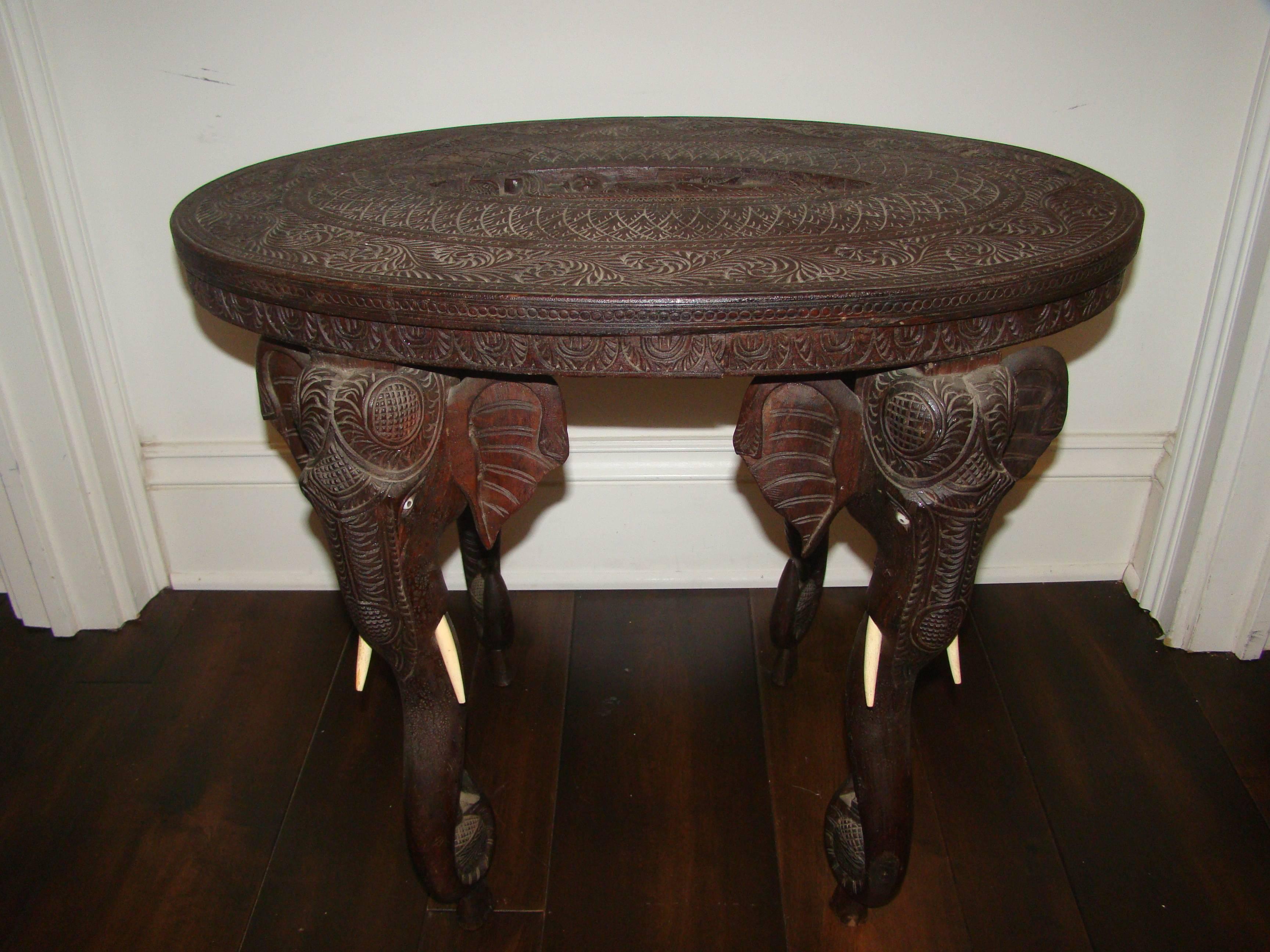 Exceptional carved rosewood Anglo Raj Indian occasional table. This amazing intricate hand-carved table depicts four elephant heads, one on each corner with faux ivory tusks and eyes. The top depicts a Buddhist theme. Truly a special and hard to
