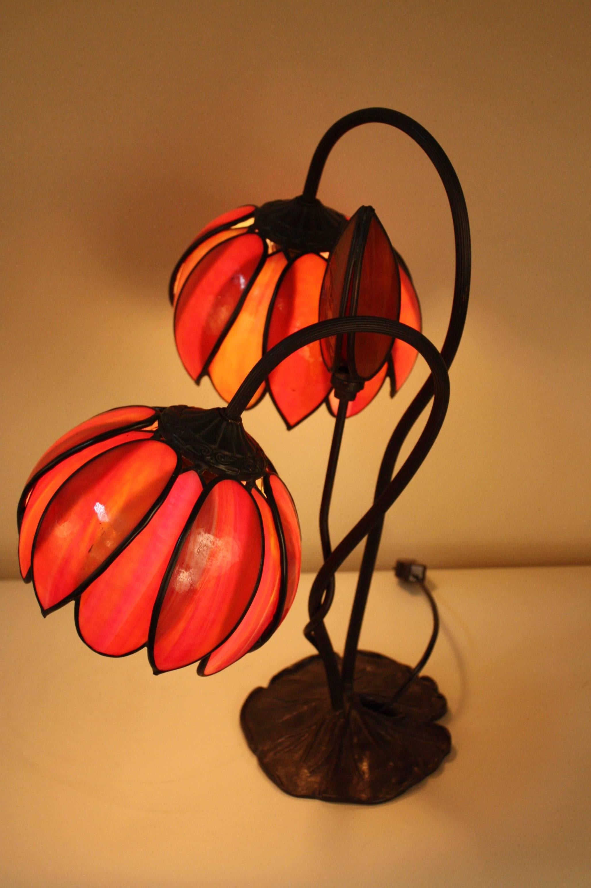 A double light, fiery/orange stained glass table lamp from the Art Nouveau period. It has a bronze lily pad base.