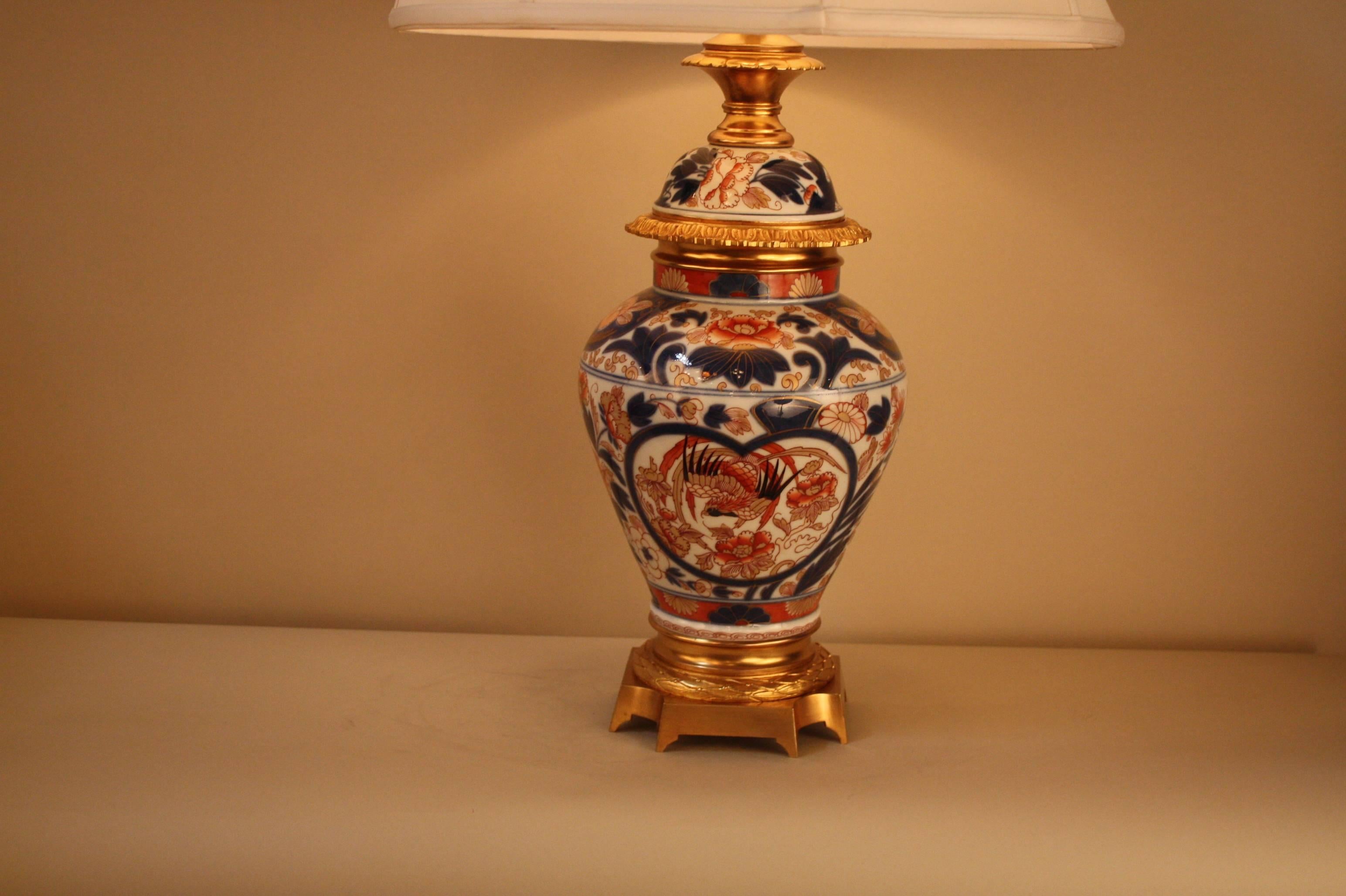 An elegant Japanese imari vase with a white background decorated with red/rust, blue and gold flowers. This beautiful 19th century vase was mounted as lamp with gilt bronze as an oil lamp which has since been electrified and fitted with a silk