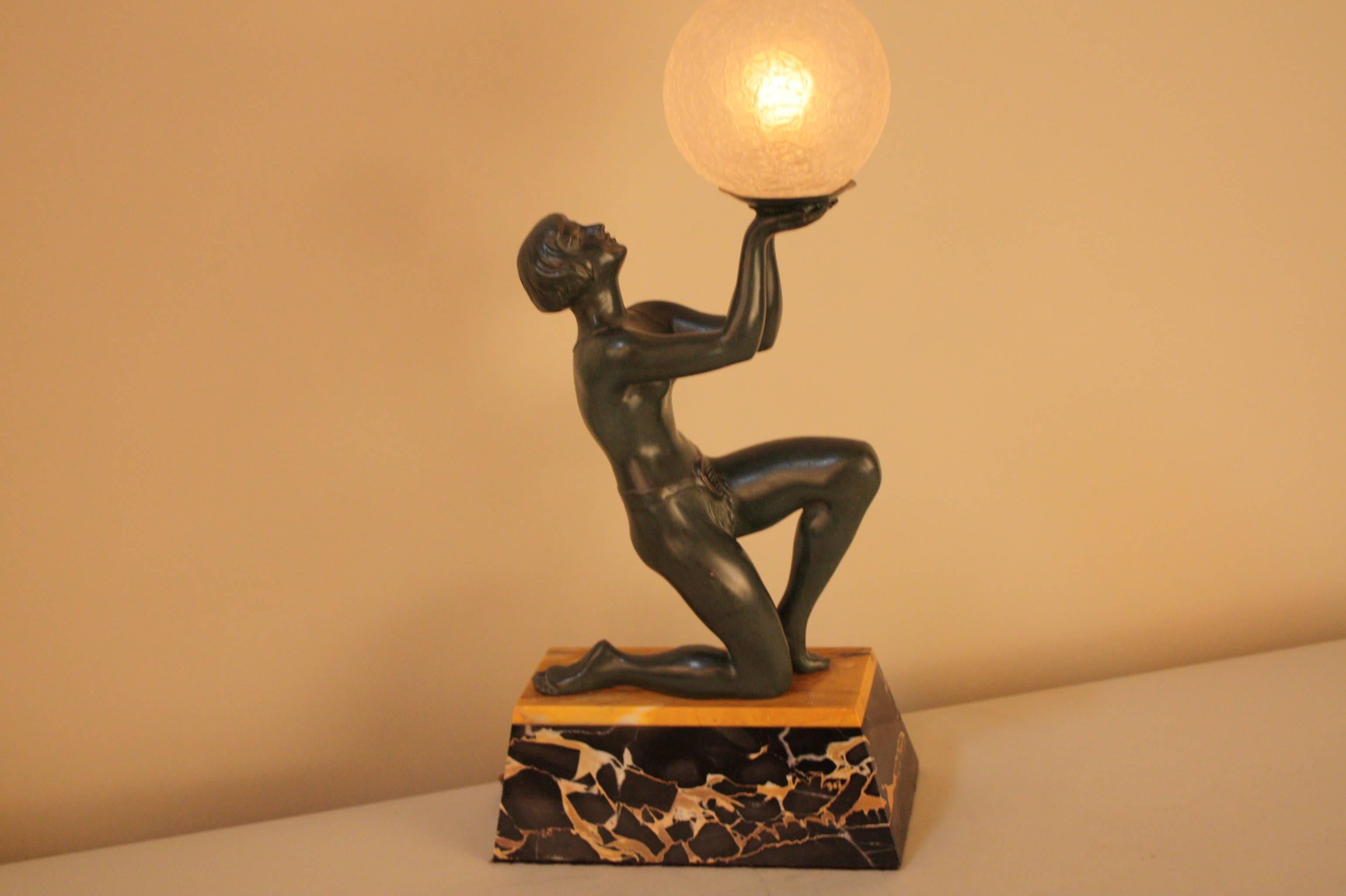 A Classic Art Deco stylized figure in dark green finish in superb detail mounted on two color marble and holding with both hands a cracker globe shade 

 