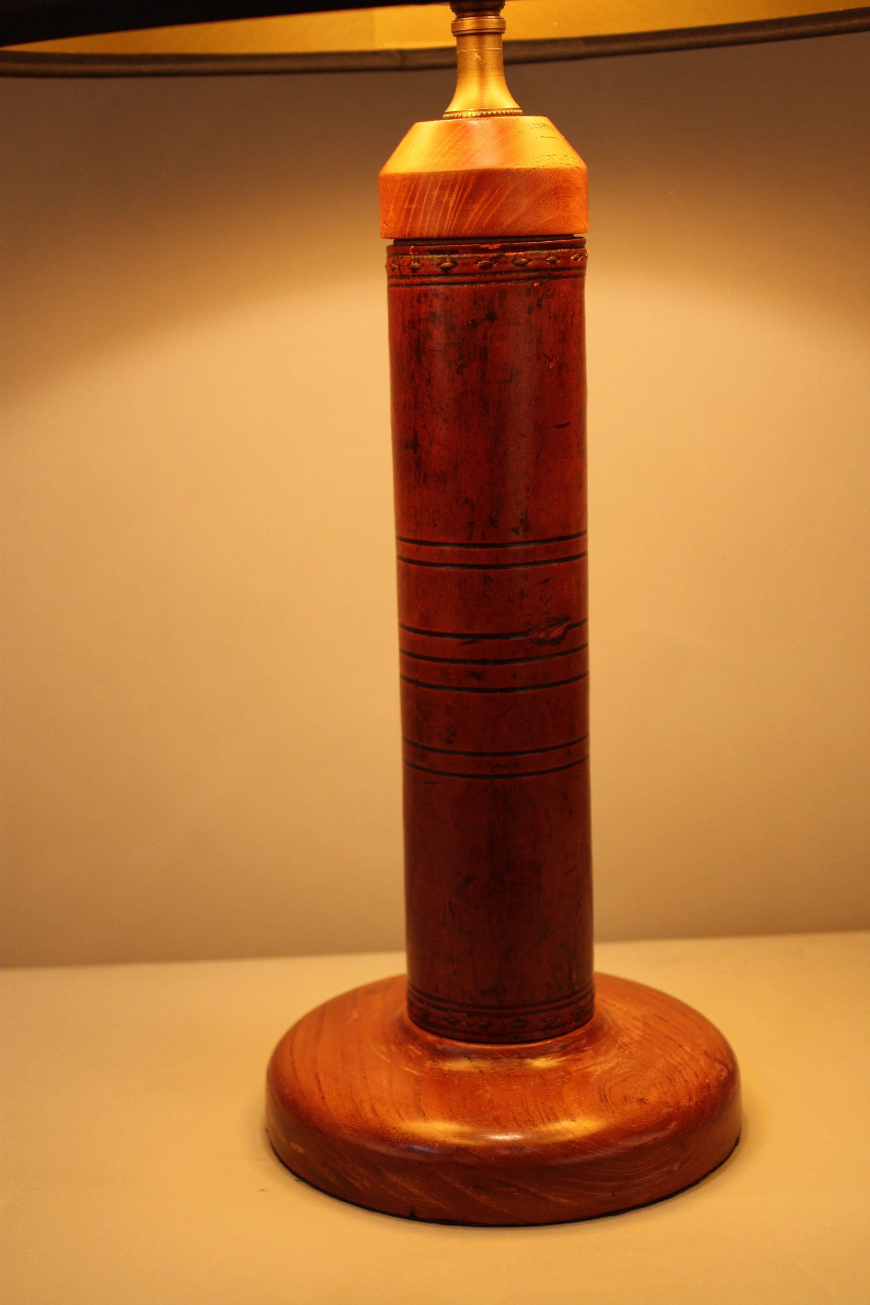 A wonderful table lamp with leather stitched column and brandy-wine cherry finish wood. This lamp is fitted with hard back black with gold liner shade.