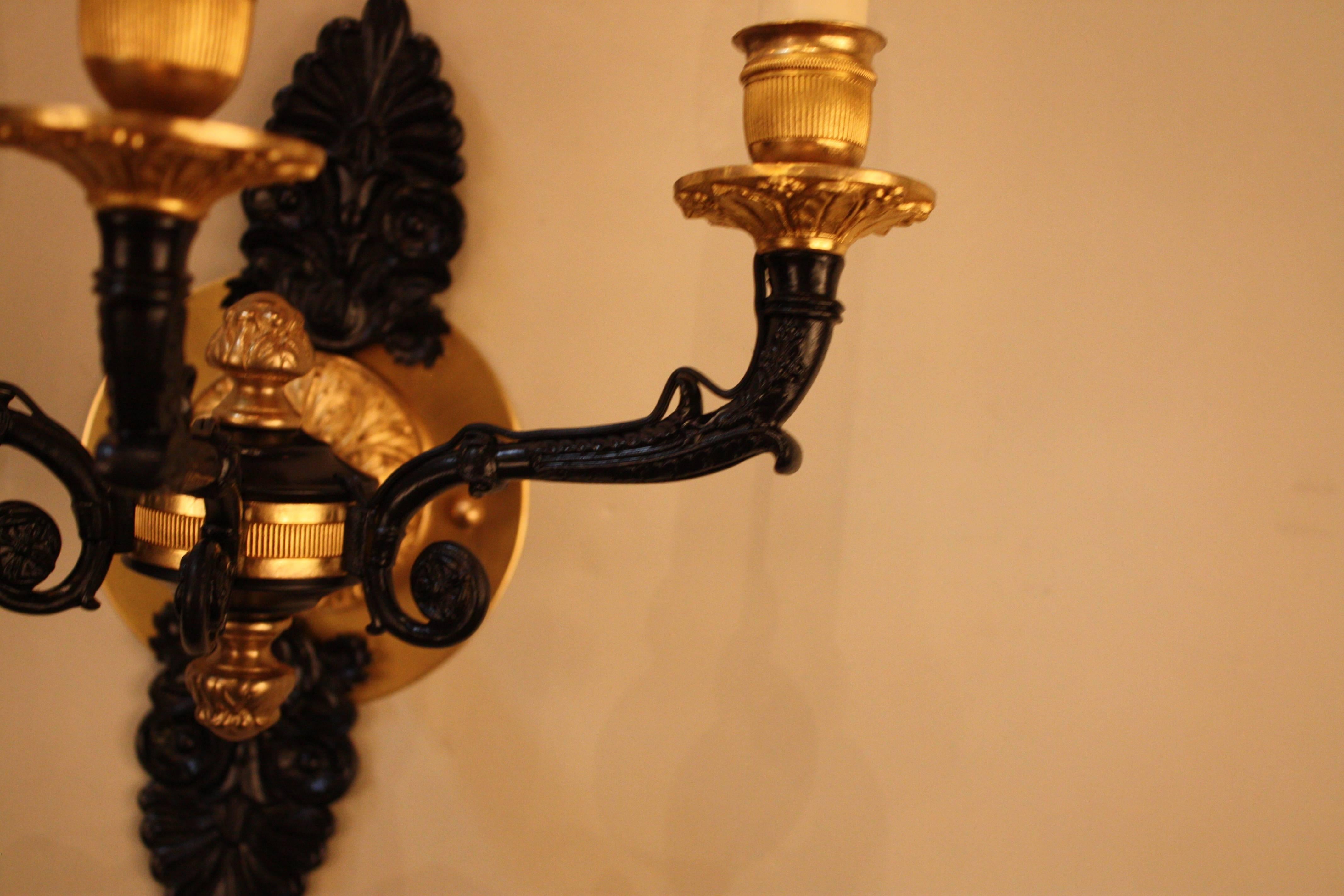 A pair of Classic design electrified three light wall sconces. This elegant pair of 19th century wall sconces are finished in golden bronze and black lacquered.