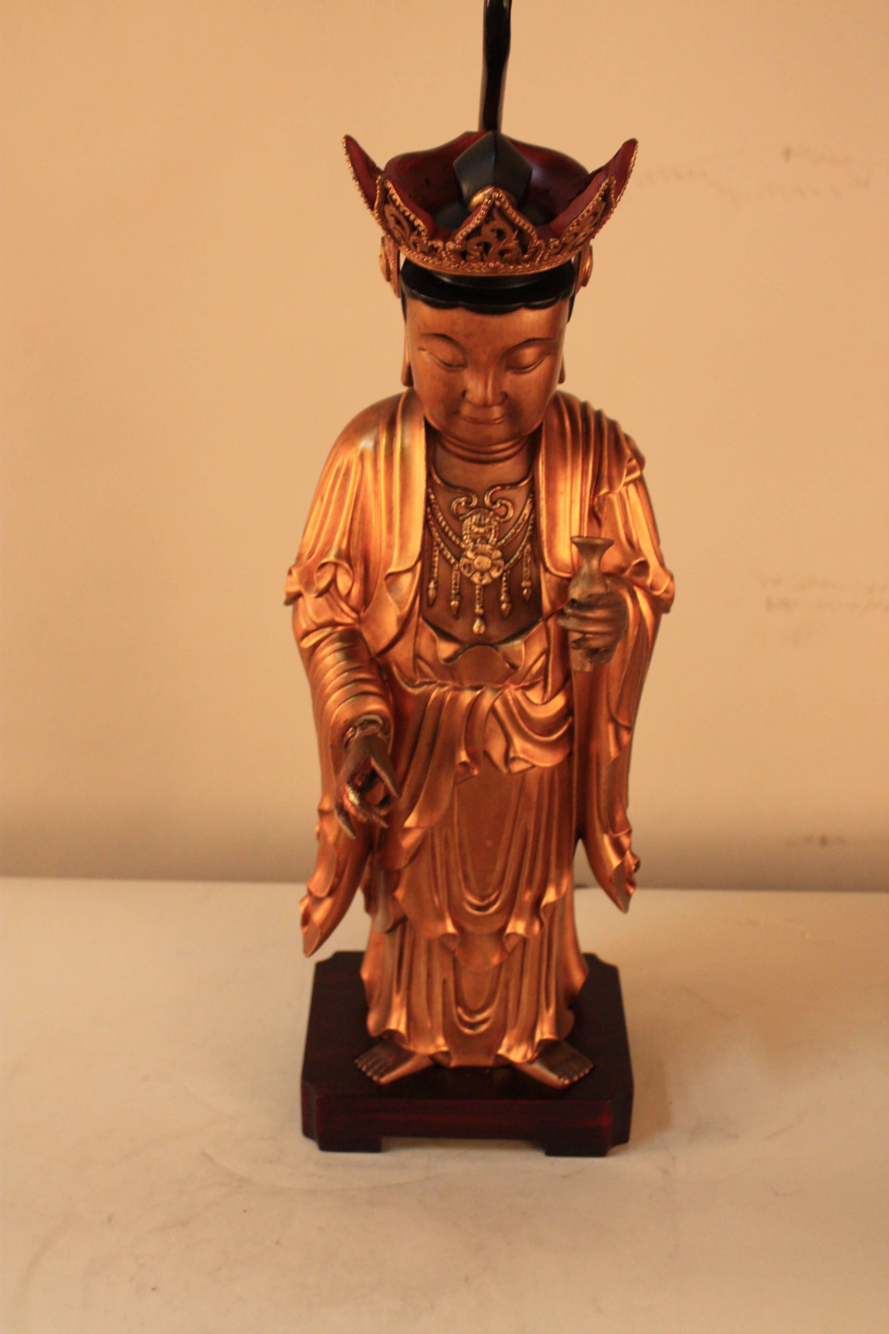 A figure of the giltwood and lacquer Buddha standing on a square rose wood base that has been customized to a table lamp.
Fabric shade and carved jade final.