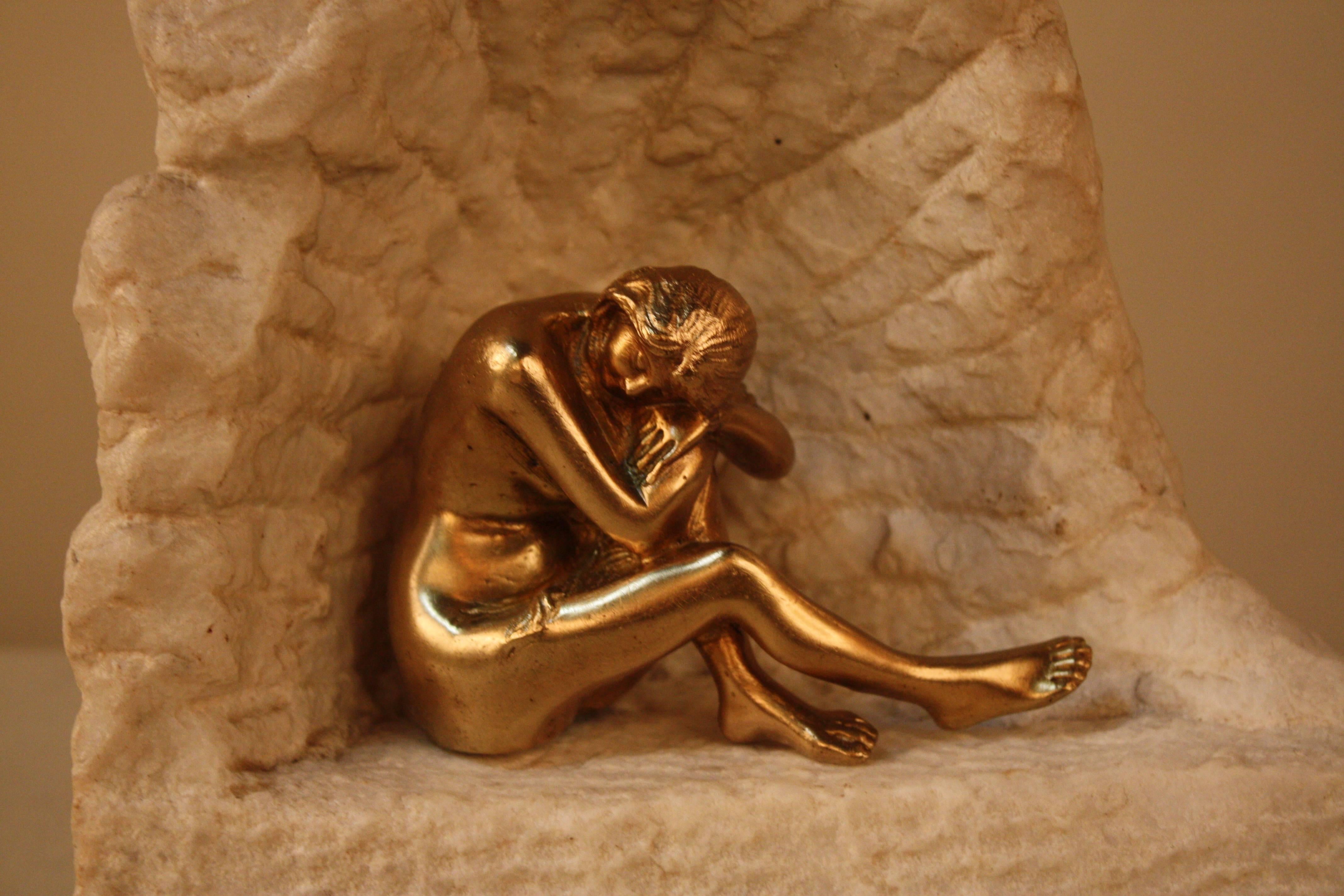 Bronze sculpture of sitting nude woman in concave rock.

 