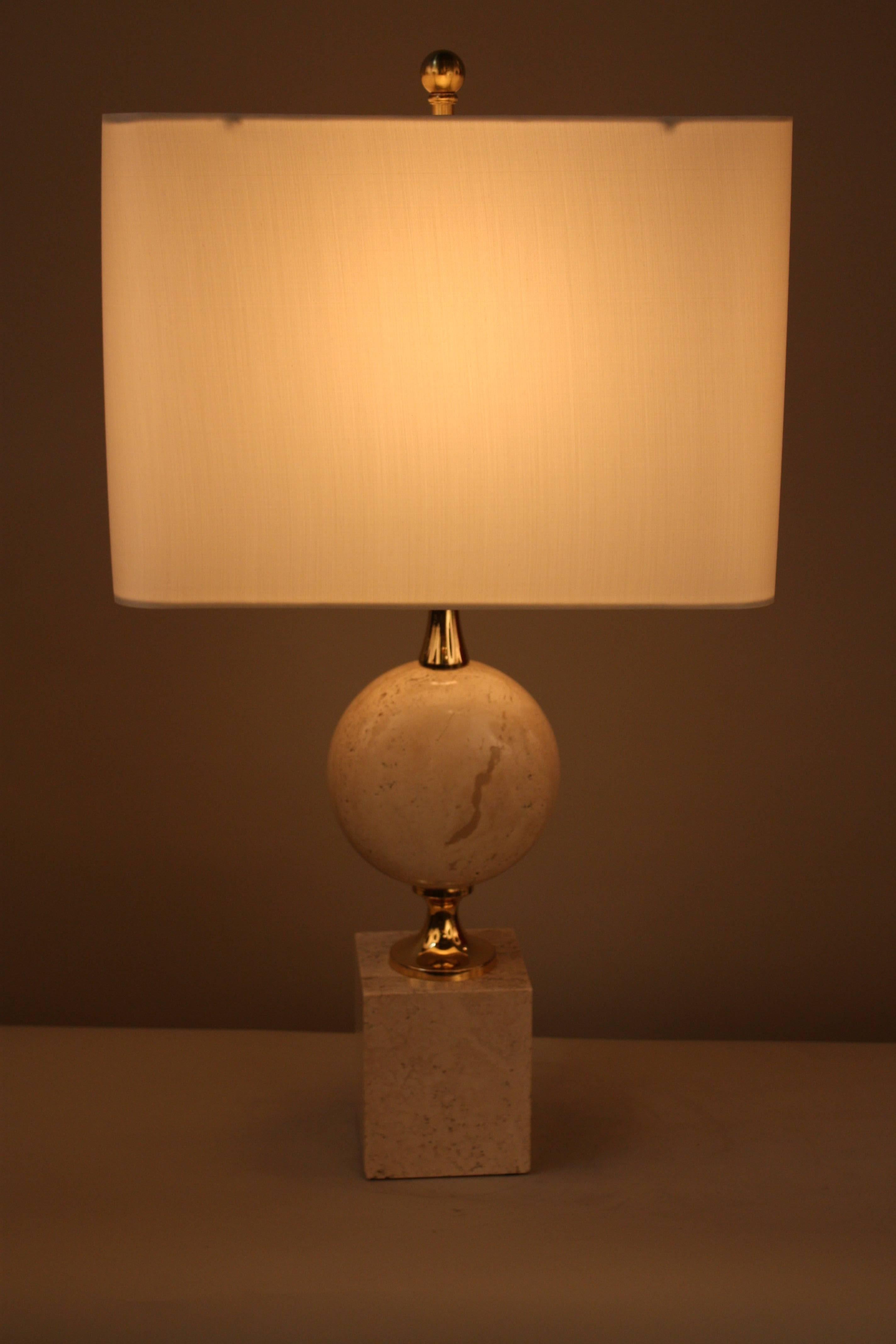 A French table lamp featuring a square base with cylinder detail. Made of beige travertine, a type of limestone. The hardware of this piece is made of gold plate over bronze, with craftsmanship attributed to Maison Barbier in the 1970s. Comes with