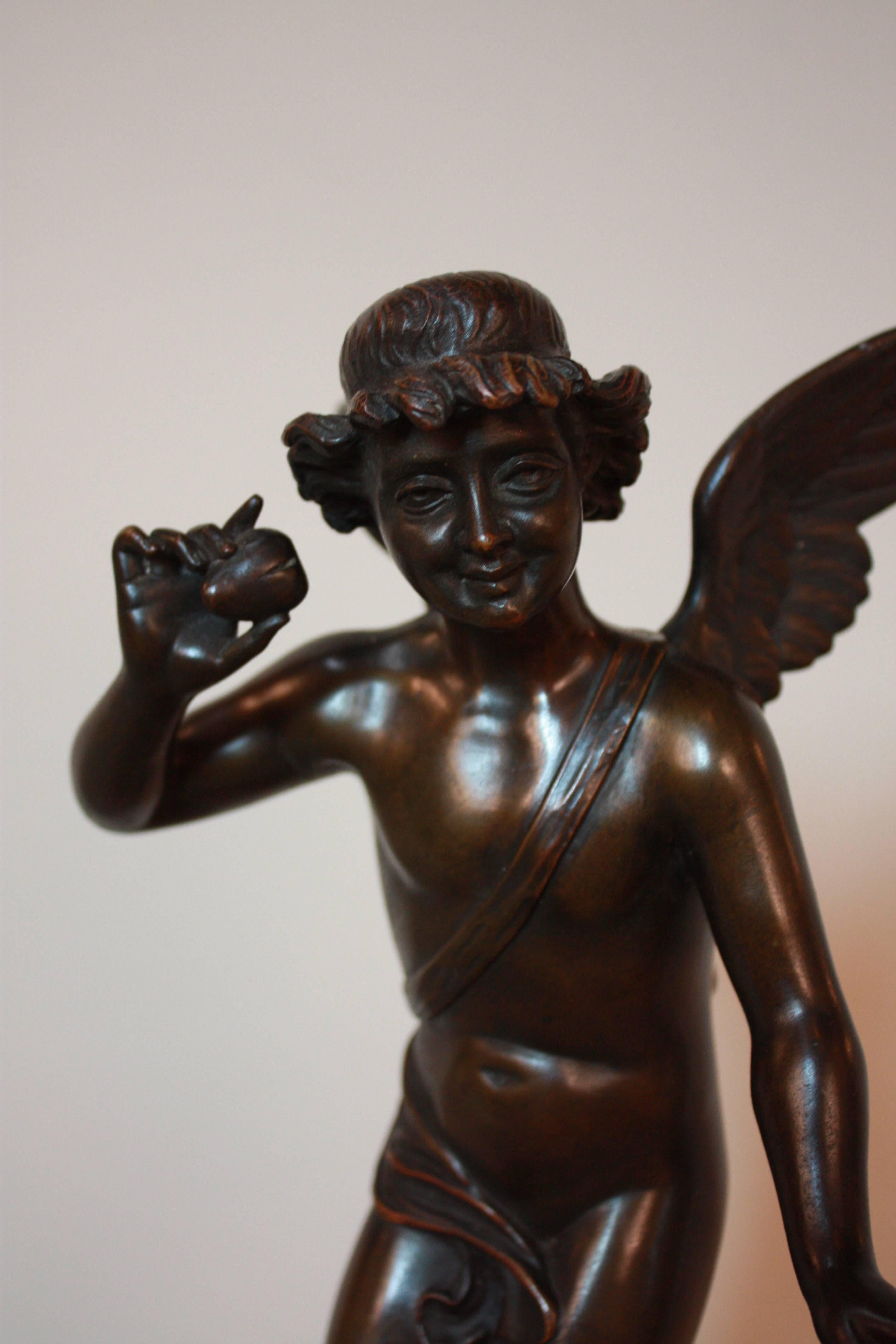 Elegant bronze sculpture of an angel holds an arrow in one hand and listens to a beating heart held in his other hand.