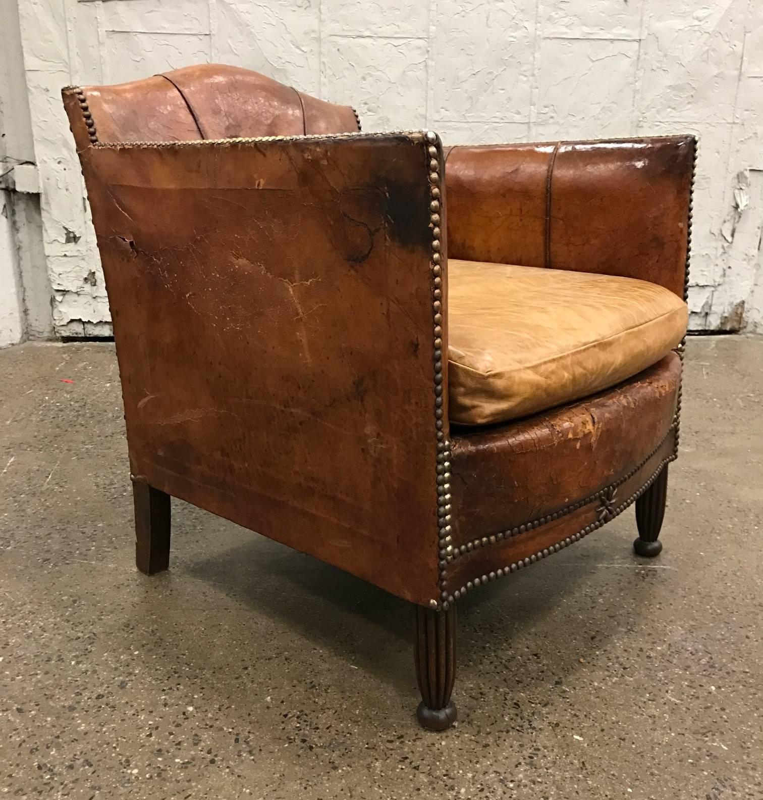 Pair of French Art Deco leather club chairs. The chairs are in vintage condition with tapered walnut legs. Has the original brass tacks to the arms and the leather is nicely worn.
