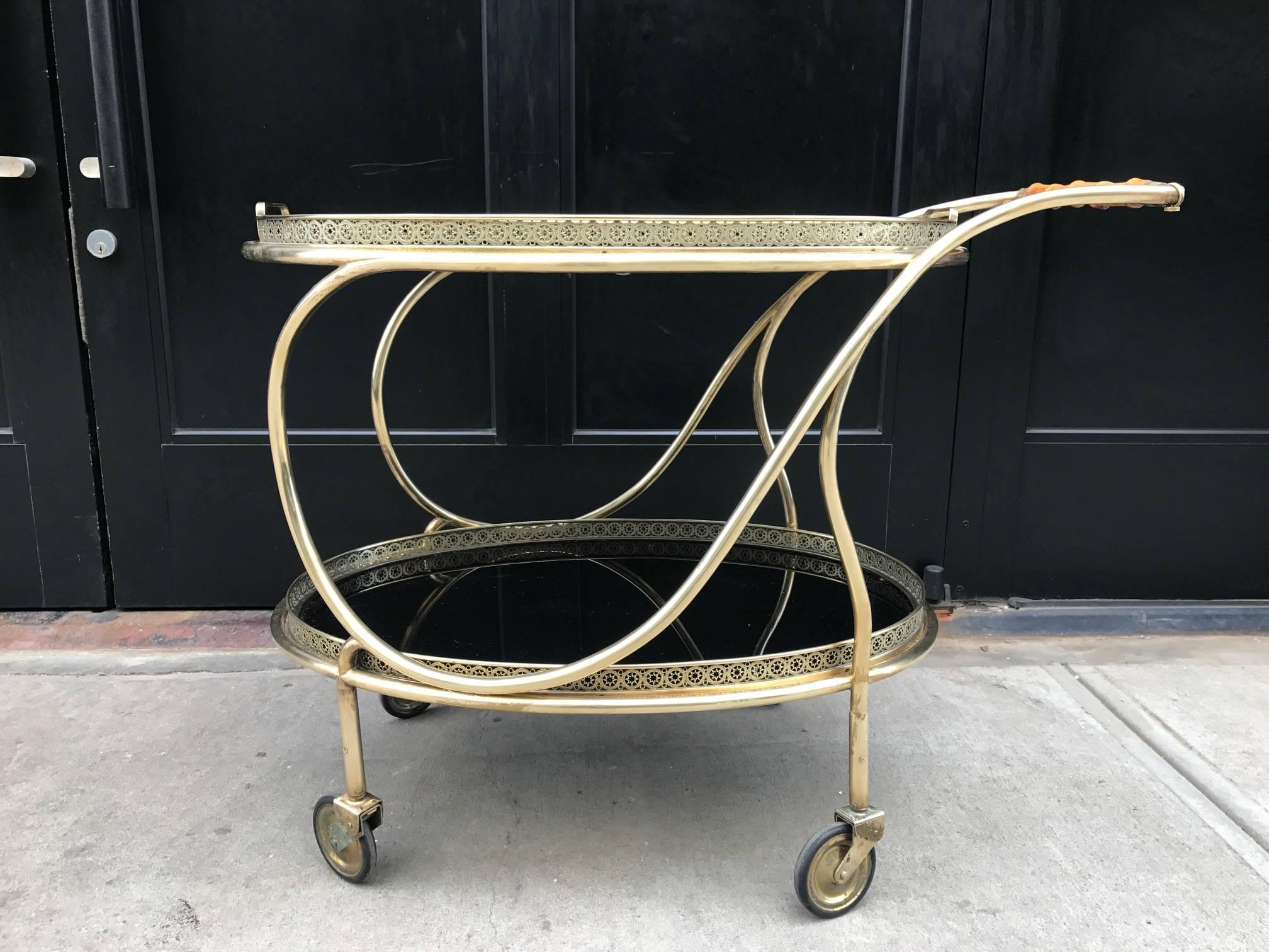 Two tiered bar cart or trolley with a decorative brass frame. Has removable serving trays. Bamboo wood handle with smoked glass tops. 