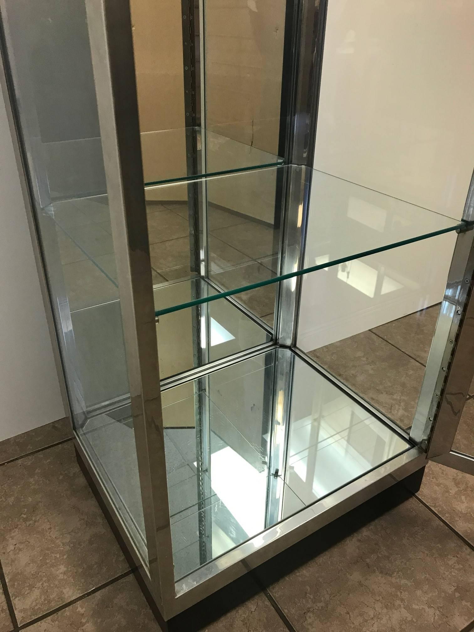 Pair of vintage aluminium and glass display cabinets. Has four glass shelves, the bottom and inside back is mirrored and also has a black lacquered wooden base. Cabinets also have a light to the inside top. Comes with the original keys to lock the