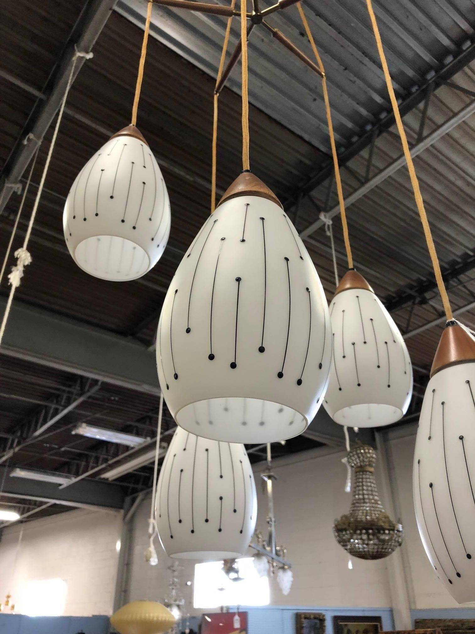 Mid-Century Modern five-pendant light fixture. Has etched glass shades. The tops of the shades are solid walnut. The ceiling cap at the top of the light fixture is brass.