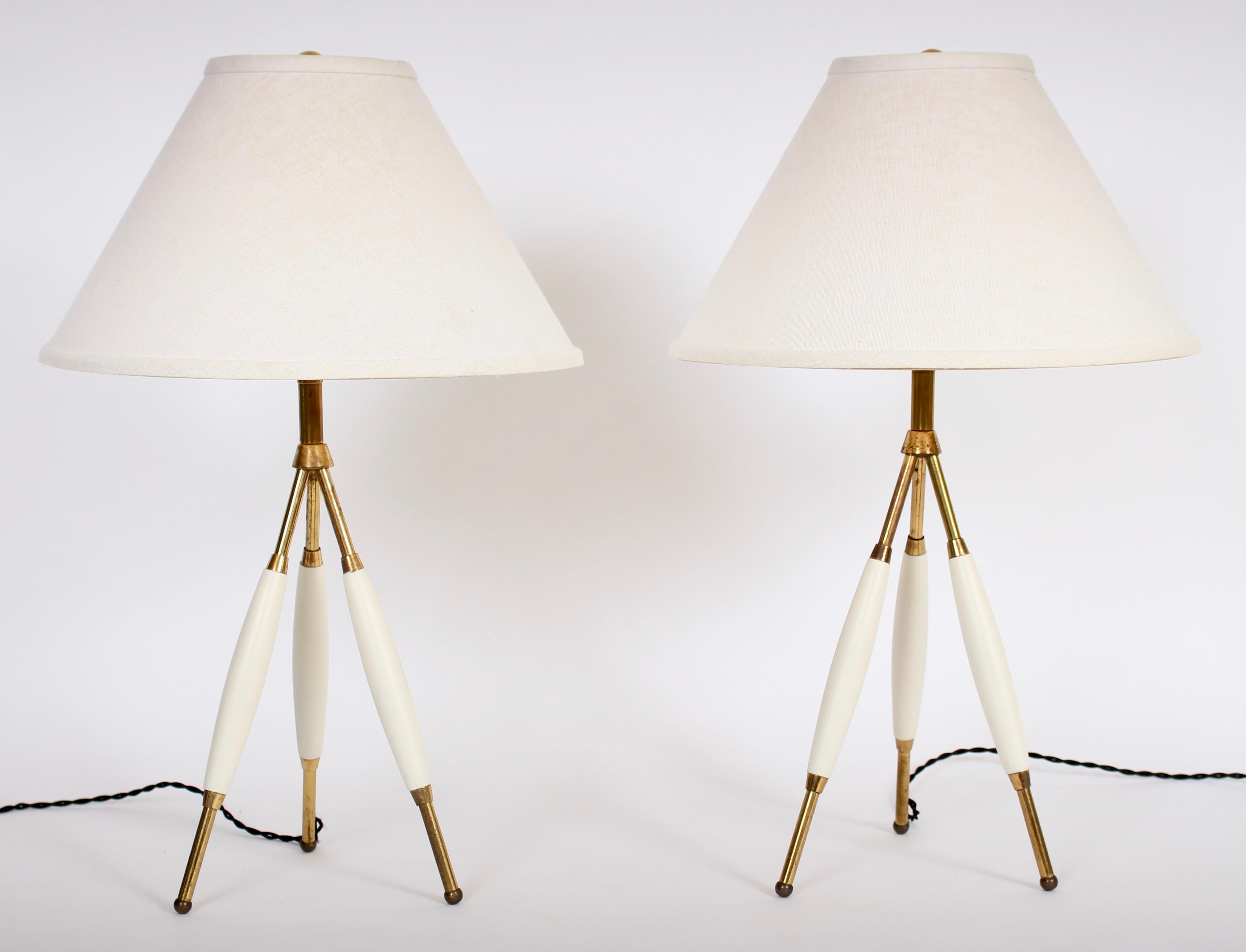 Classic Gerald Thurston for Lightolier Co. brass and off-white enameled wood tripod lamps. Featuring three patinated brass tubular rods per, applied rounded wooden details and brass ball feet. Shades shown for display only (9 H x 5 D top x 14 D