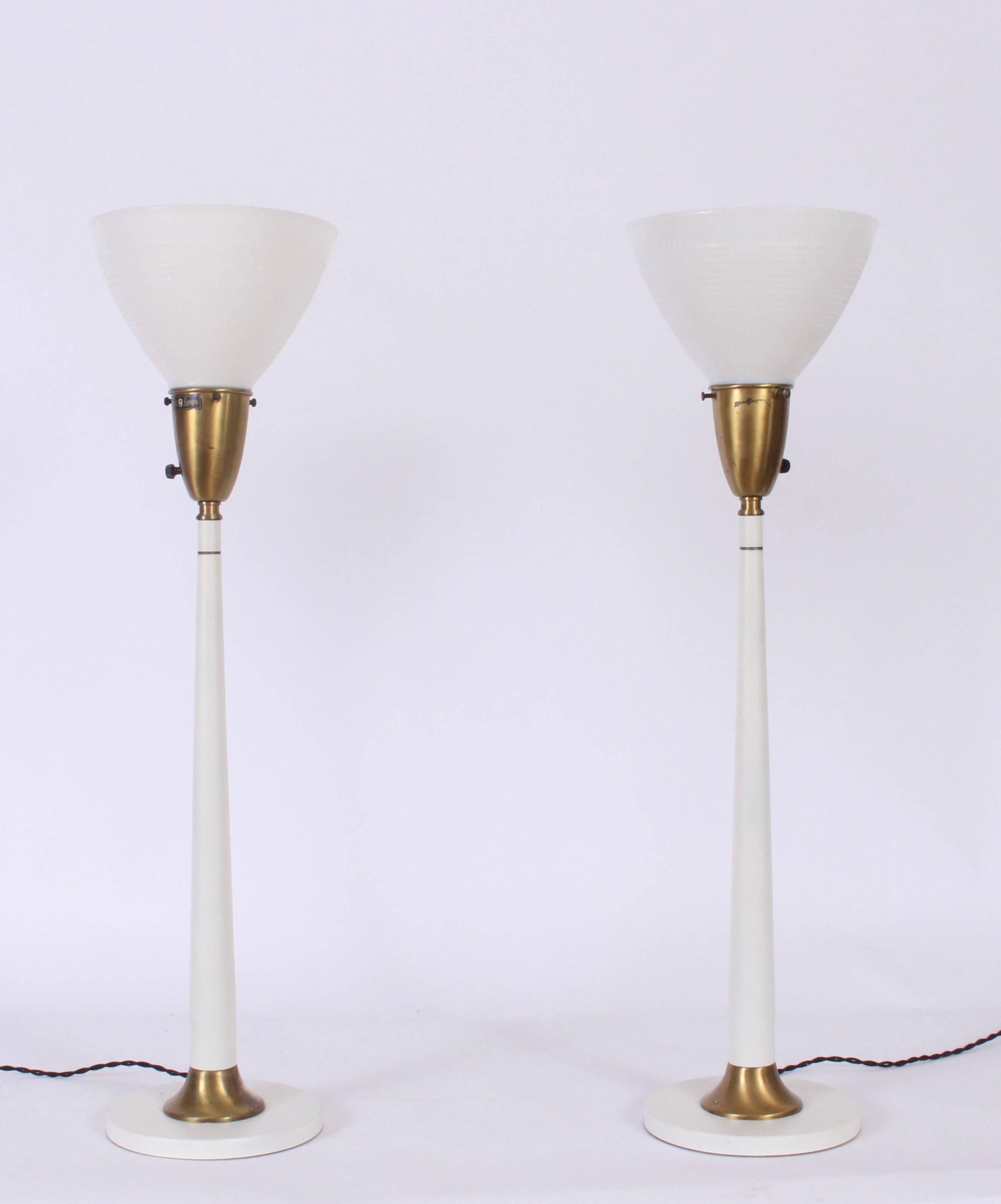 Pair of Rembrandt Lamp Company off white enamel and brass lamps with white milk glass shades. Featuring slim white candlesticks, and White glass liner shades on Round base. Patinated brass details. Small footprint. 24 H to top of socket. Shades