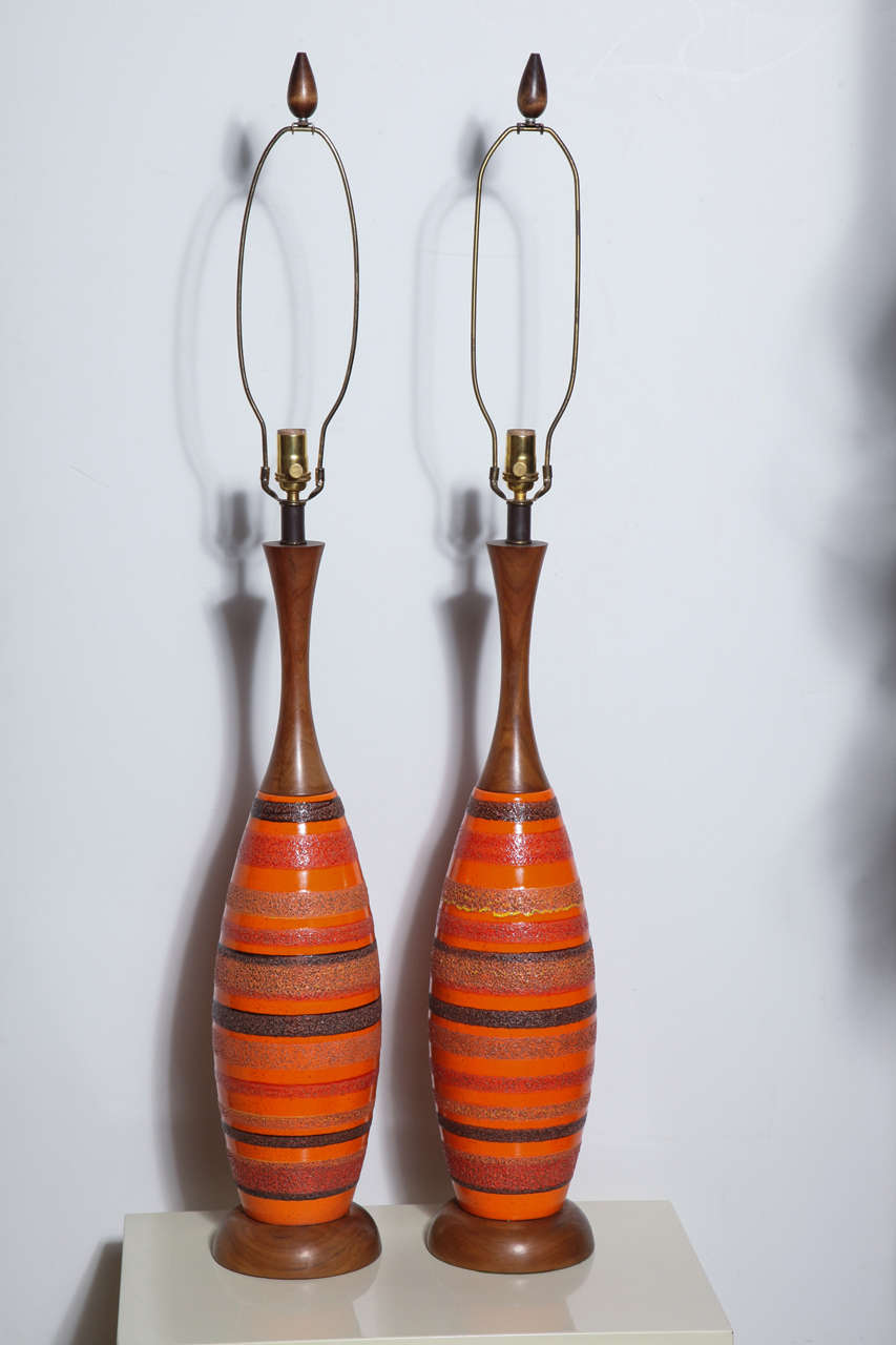 Substantial pair of Raymor attributed walnut and orange banded glazed ceramic table lamps. Featuring an elongated bowling pin form with walnut neck and base, glazed orange textured ceramic with pumice banded striping in red, yellow, brown, black and