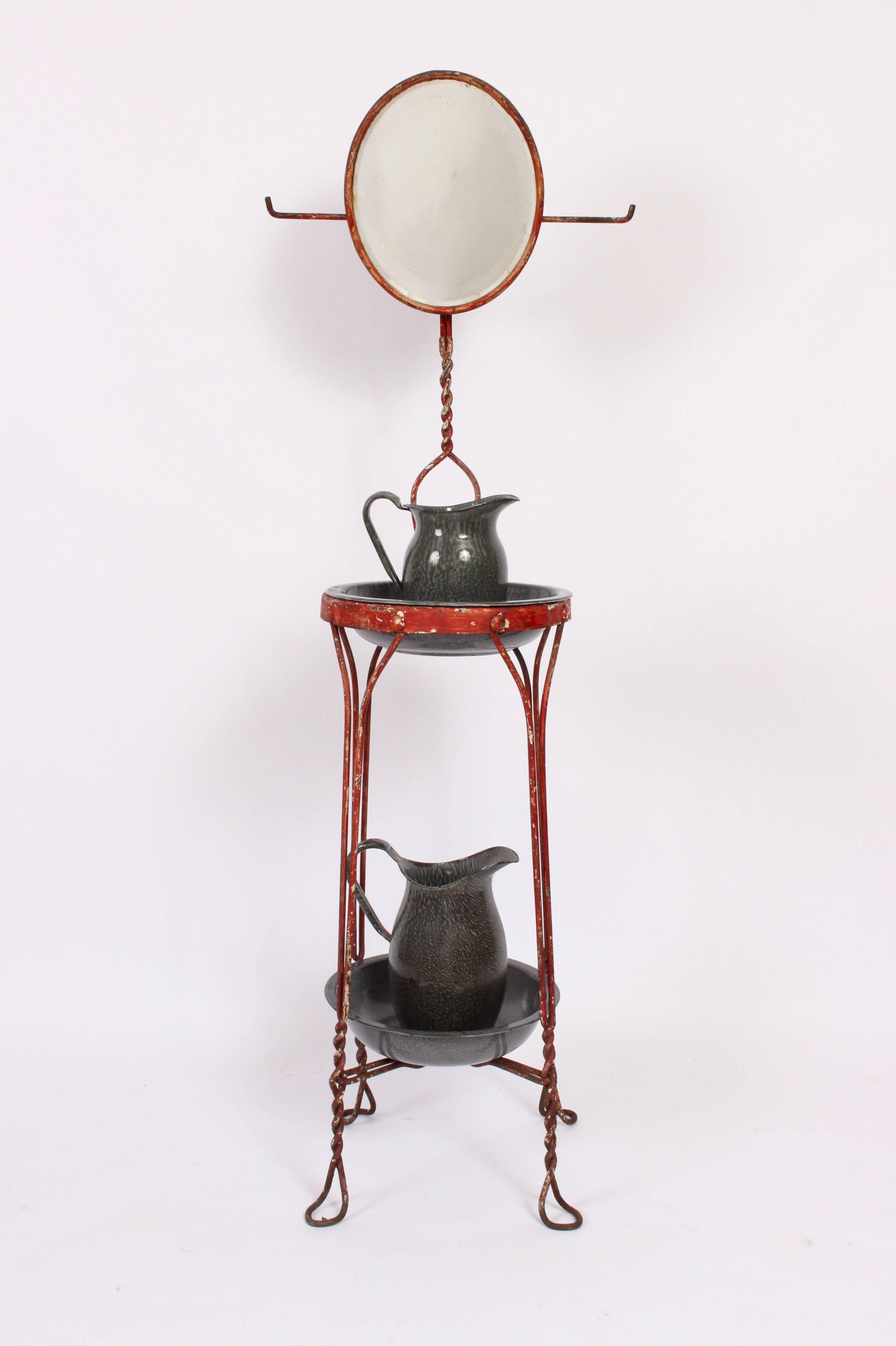 Late Victorian Painted Metal Stand with beveled Mirror.  The wash stand, shaving stand features a twisted metal wire framework, beveled oval mirror, two towel racks, two shelves, two gray enameled graniteware basins.  Shown with two dark gray