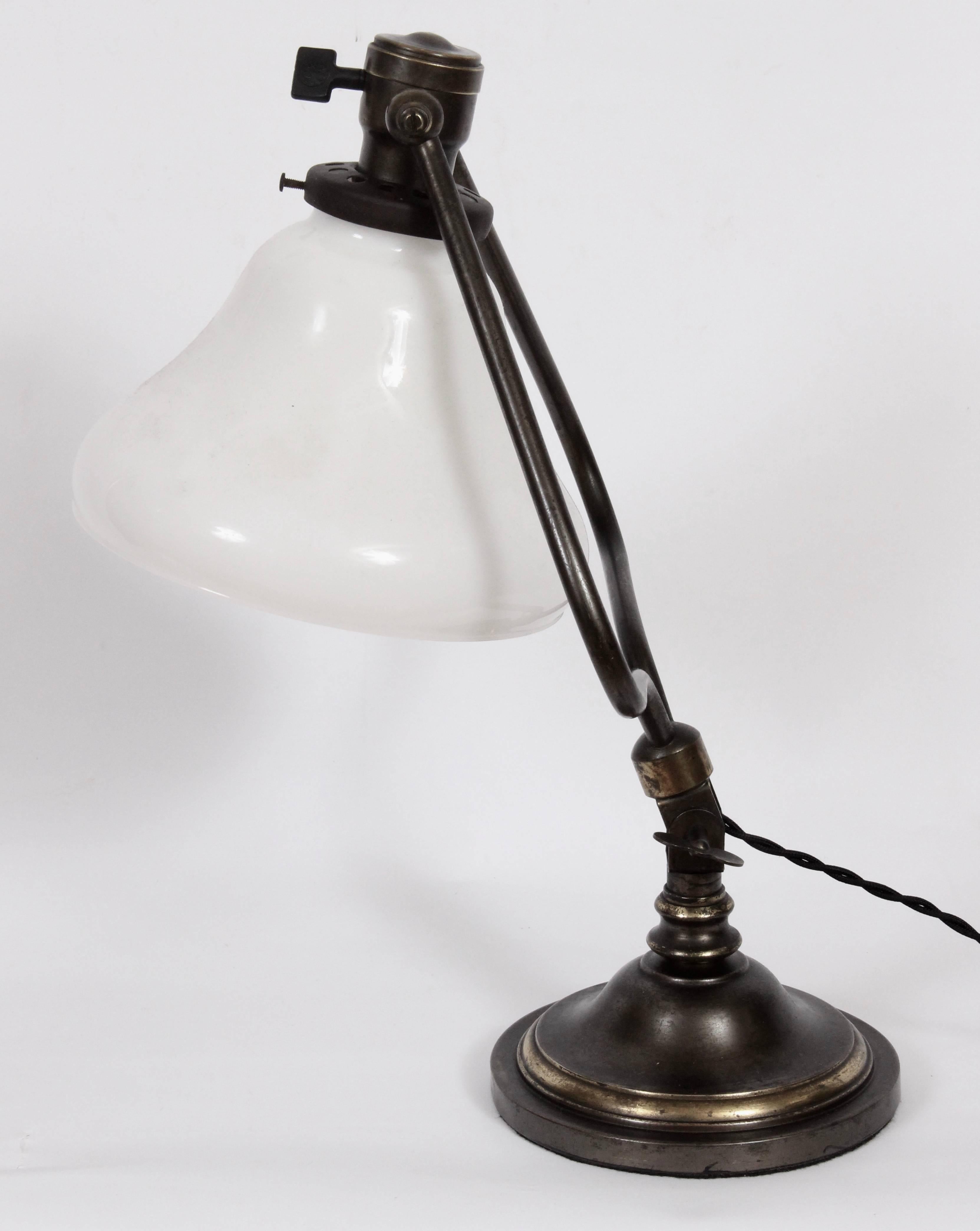 Early electric Edwardian tiffany style all brass harp table lamp with white milk glass bell shade attributed to Bradley and Hubbard, circa 1910. Featuring a patinated brass with bronze appearance with fully articulating shade which tilts and turns,